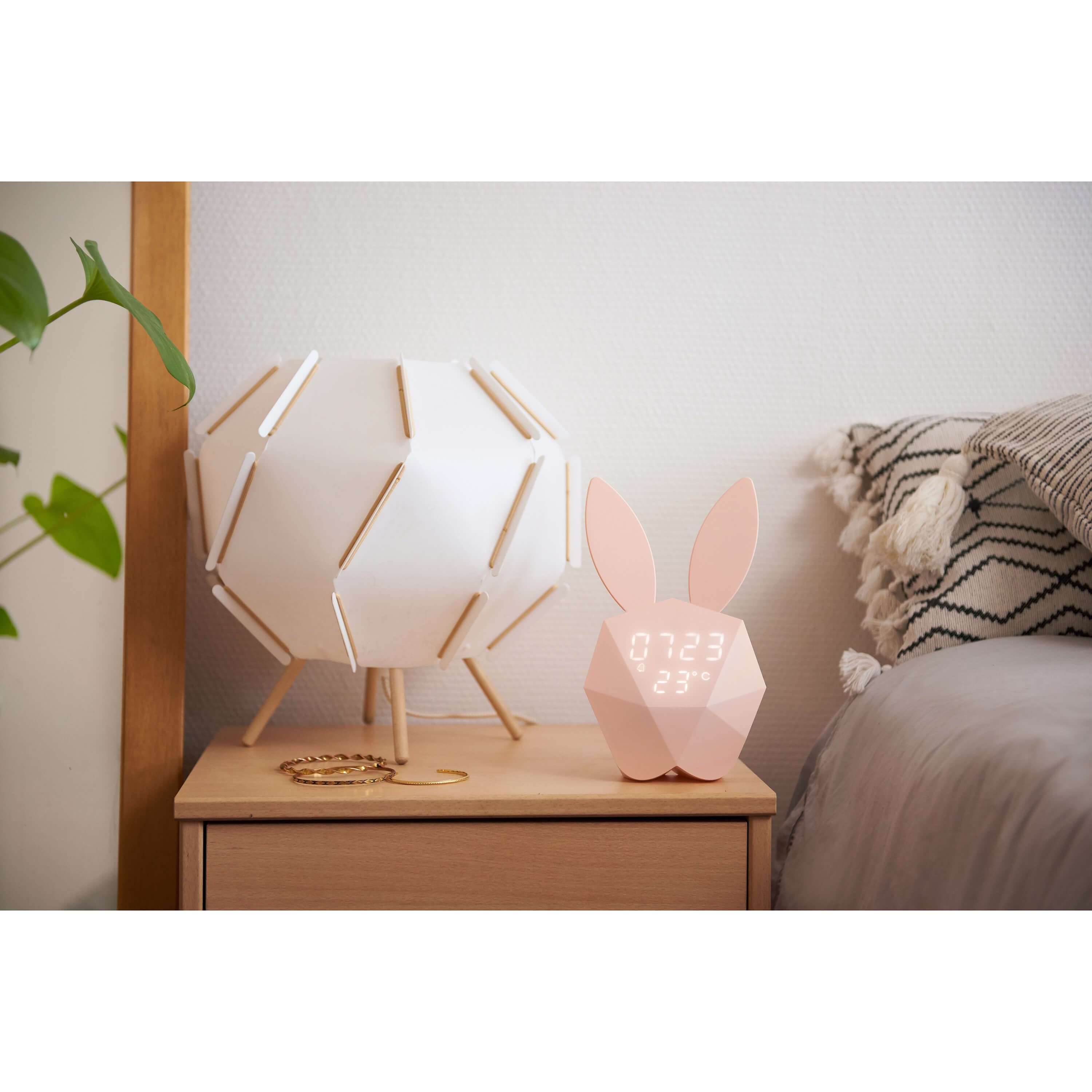 Rosa Kaninchen-Wecker auf einem Nachttisch. Eine Lampe und Schmuck sind ebenfalls sichtbar.