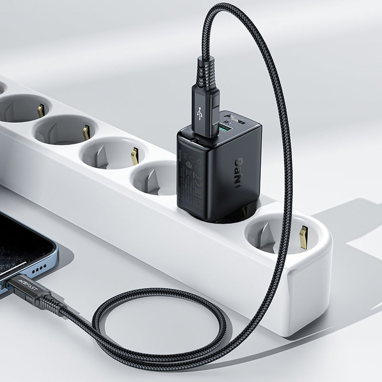 Schwarzes Telefonladegerät an weißer Steckdosenleiste. Ein anderes Kabel ist mit einem Telefon verbunden.