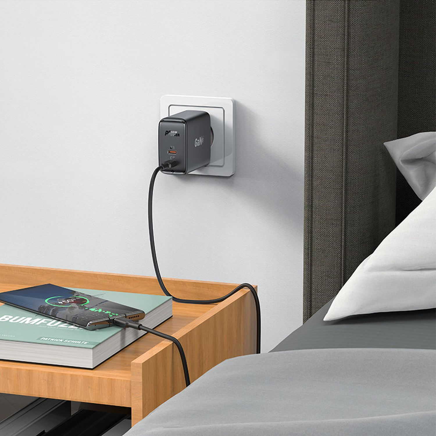 Ein schwarzes Ladegerät ist an der Wand angeschlossen. Ein Telefon lädt auf einem Holztisch neben einem Bett.