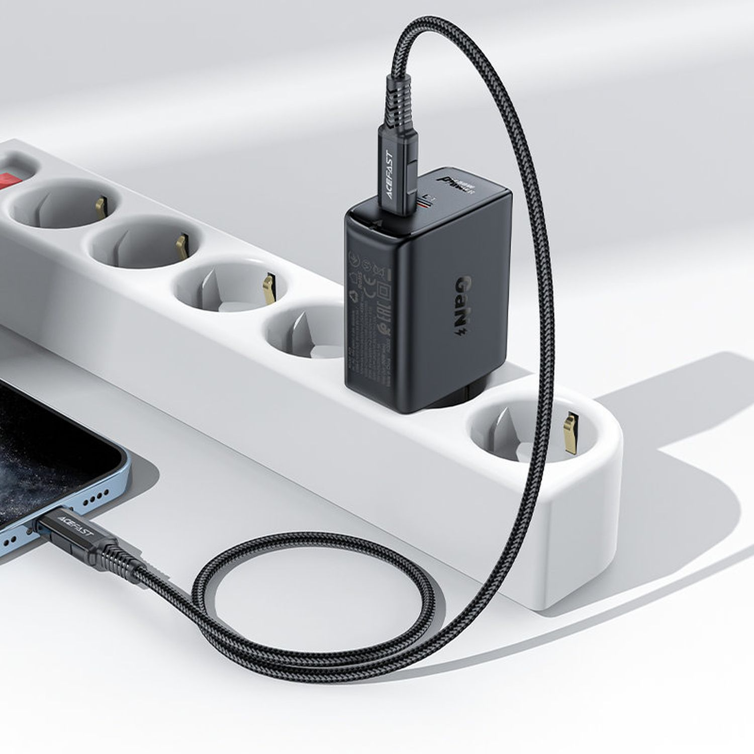 Schwarzes Ladegerät an einer weißen Steckdosenleiste. Ein schwarzes Ladekabel ist an ein Telefon angeschlossen.