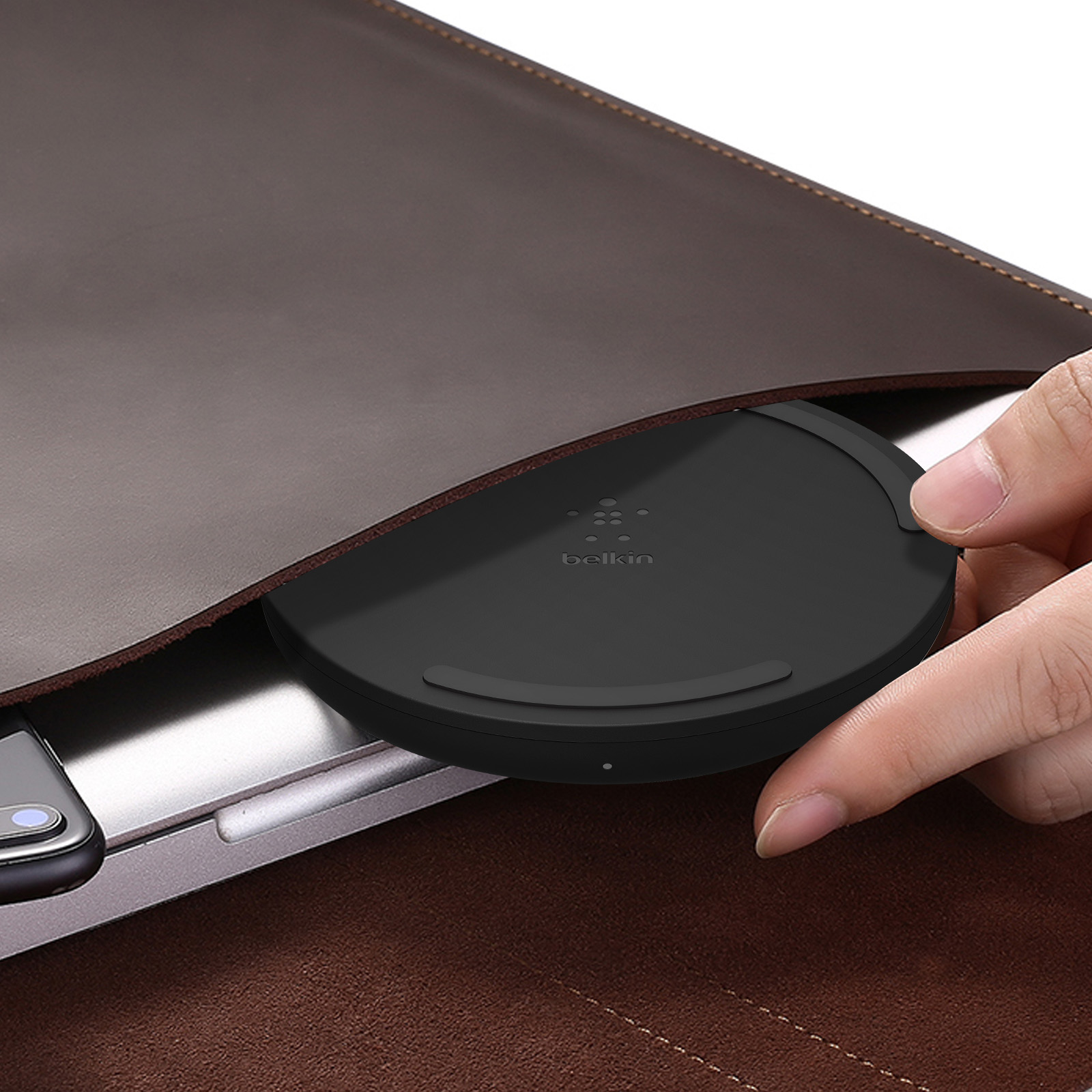 Schwarzes kabelloses Ladegerät in einem braunen Etui. Hand greift danach.