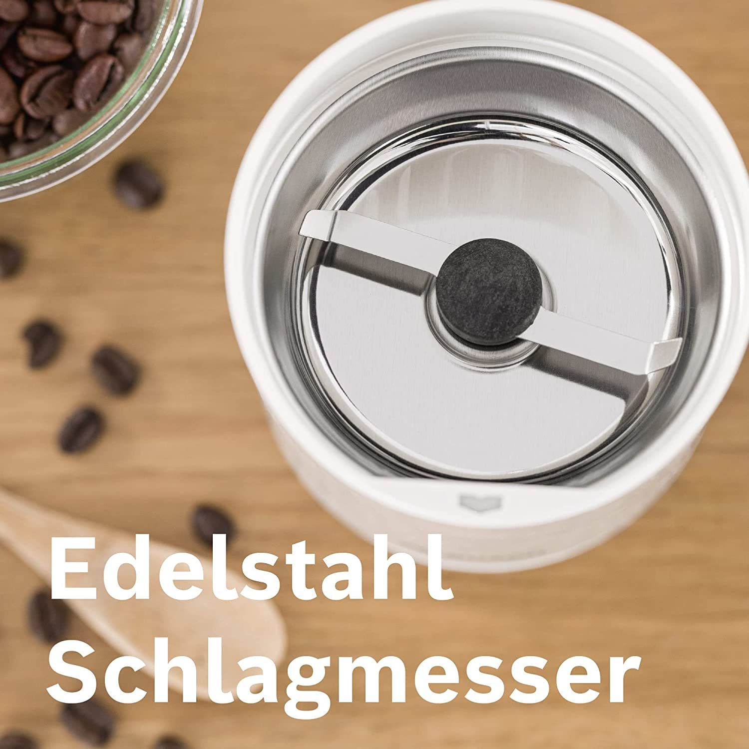 Innenansicht der Kaffeemühle. Klinge in der Mitte, Kaffeebohnen auf der Holzoberfläche. Text: Edelstahl Schlagmesser.