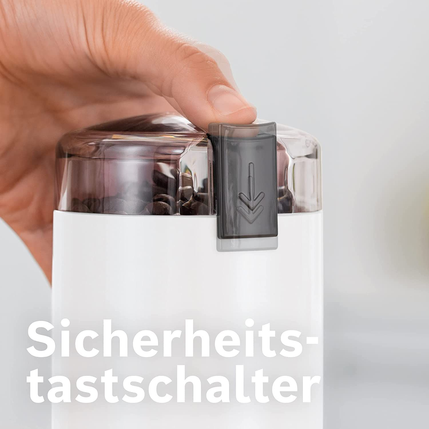 Hand drückt einen Sicherheitsknopf auf einer weißen und grauen Kaffeemühle.
