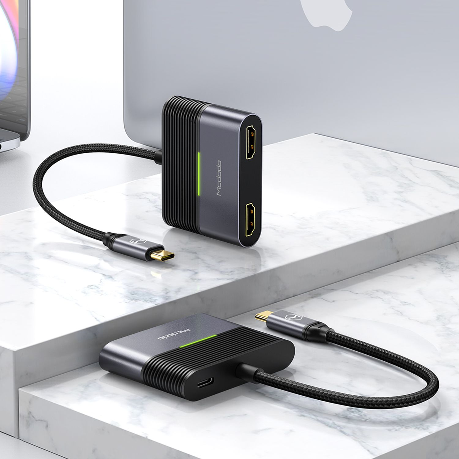 Zwei graue USB-C-Multiport-Adapter auf einer Marmoroberfläche. Einer ist über ein Kabel mit einem Gerät verbunden. Grüne Kontrollleuchten.