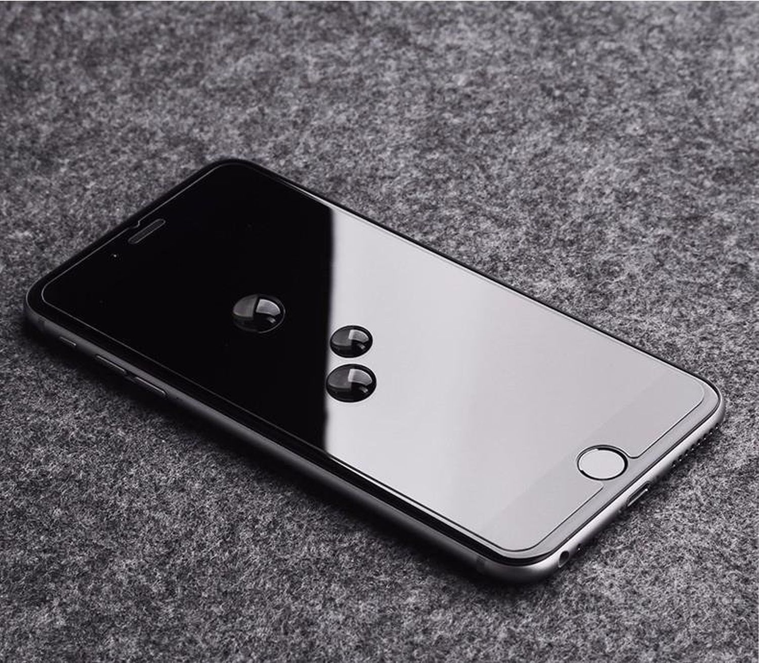 Ein schwarzes Smartphone auf grauer Oberfläche mit Wassertropfen auf dem Bildschirm.
