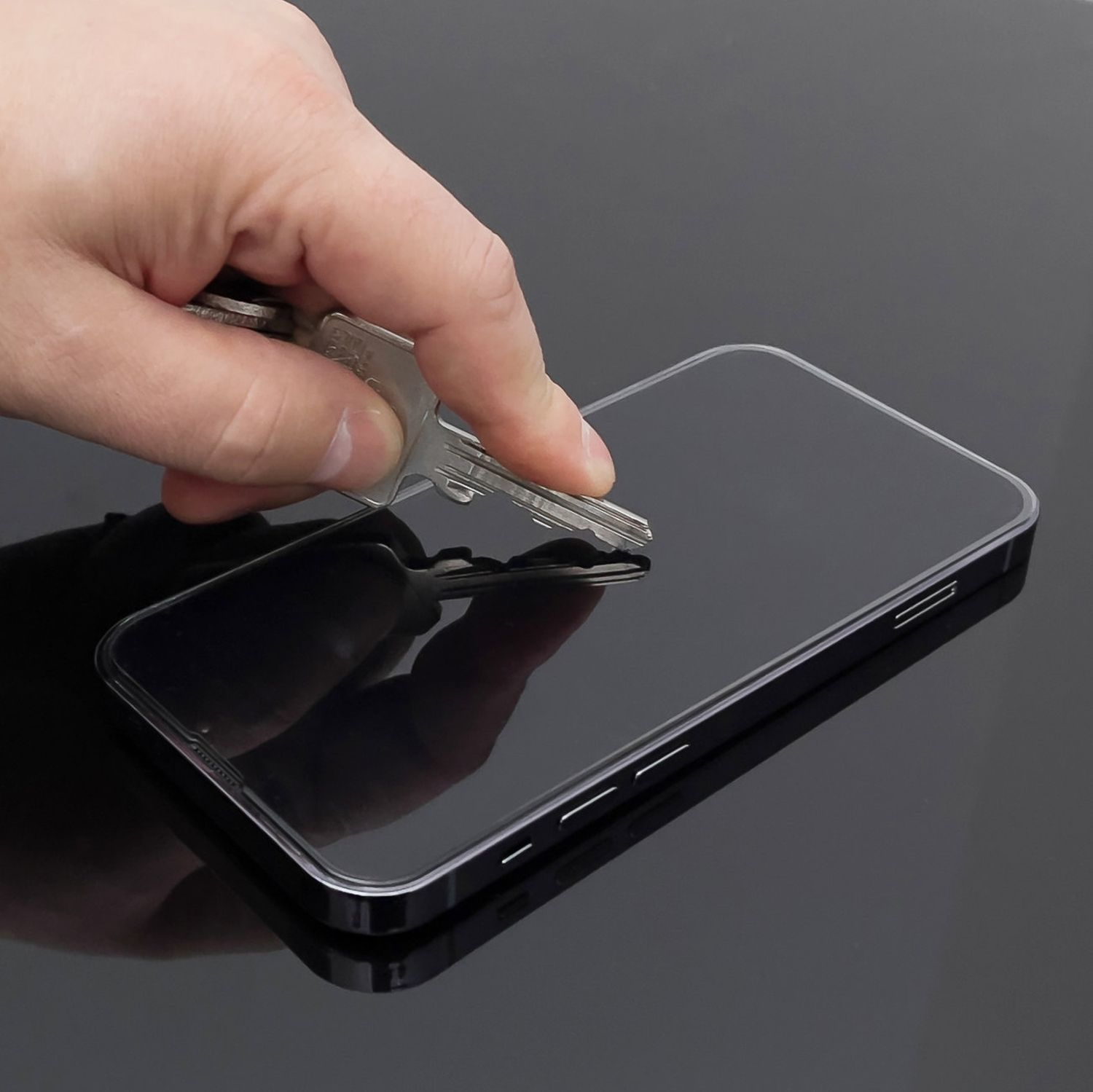 Eine Hand testet mit einem Schlüssel einen Displayschutz für ein Telefon.