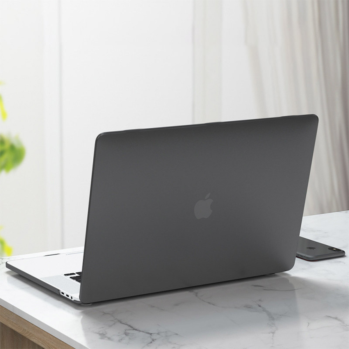 Dunkelgrauer Laptop auf Marmor. Apple-Logo sichtbar. Ein Smartphone liegt daneben.