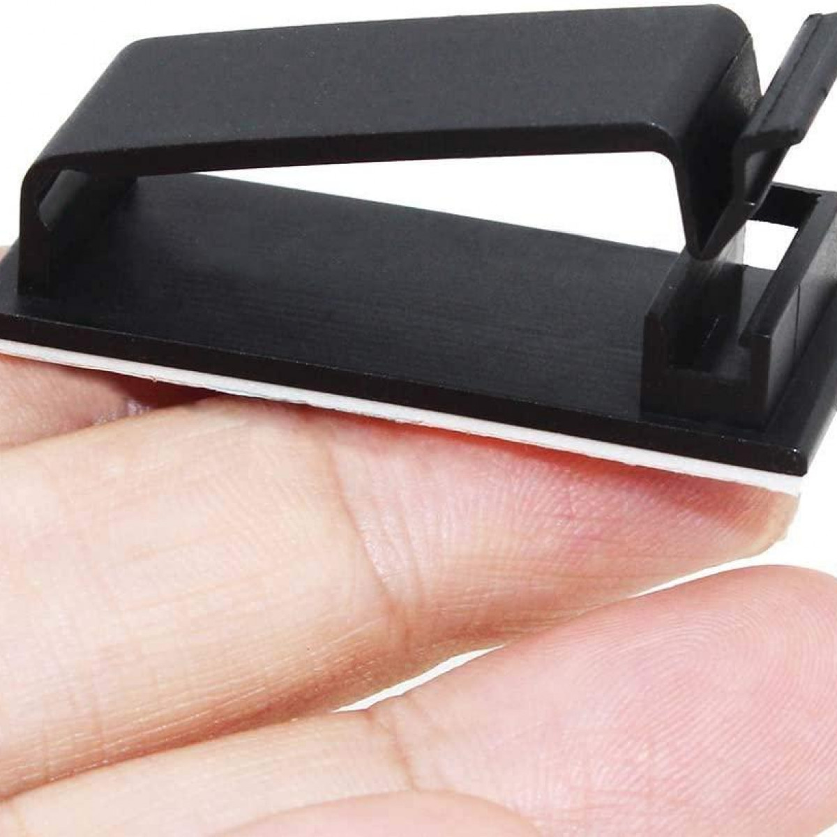Black cable clip with adhesive backing, mounted on a hand, showing the clip's design and function.