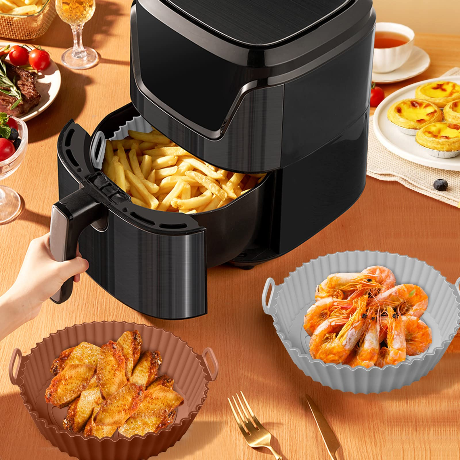 Heißluftfritteuse mit frittierten Speisen, Garnelen und Hühnerflügeln auf dem Tisch.
