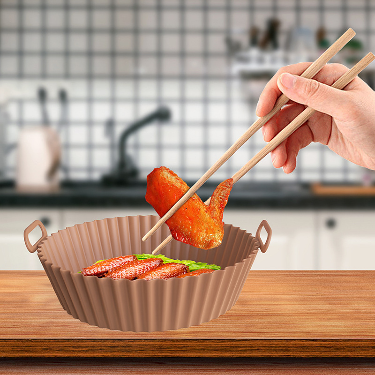 Hand mit Essstäbchen, die ein gekochtes Hähnchenflügel aus einem braunen, gerüschten Silikon-Frittierkorb aufnehmen.