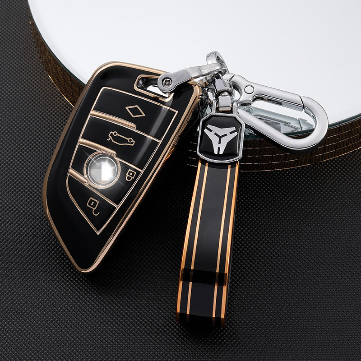 Schwarzer und goldener Autoschlüssel mit Schlüsselanhänger und silbernem Karabinerhaken, auf reflektierender Oberfläche.