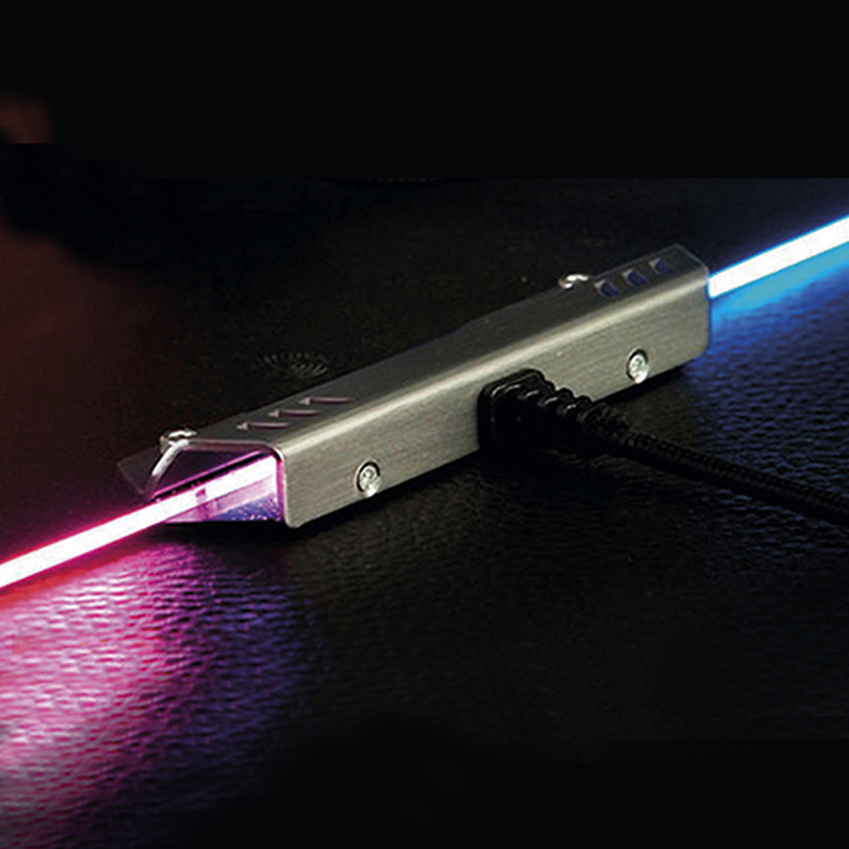 Dispositivo plateado que emite rayos de luz rosa y azul. El dispositivo tiene un cable negro.