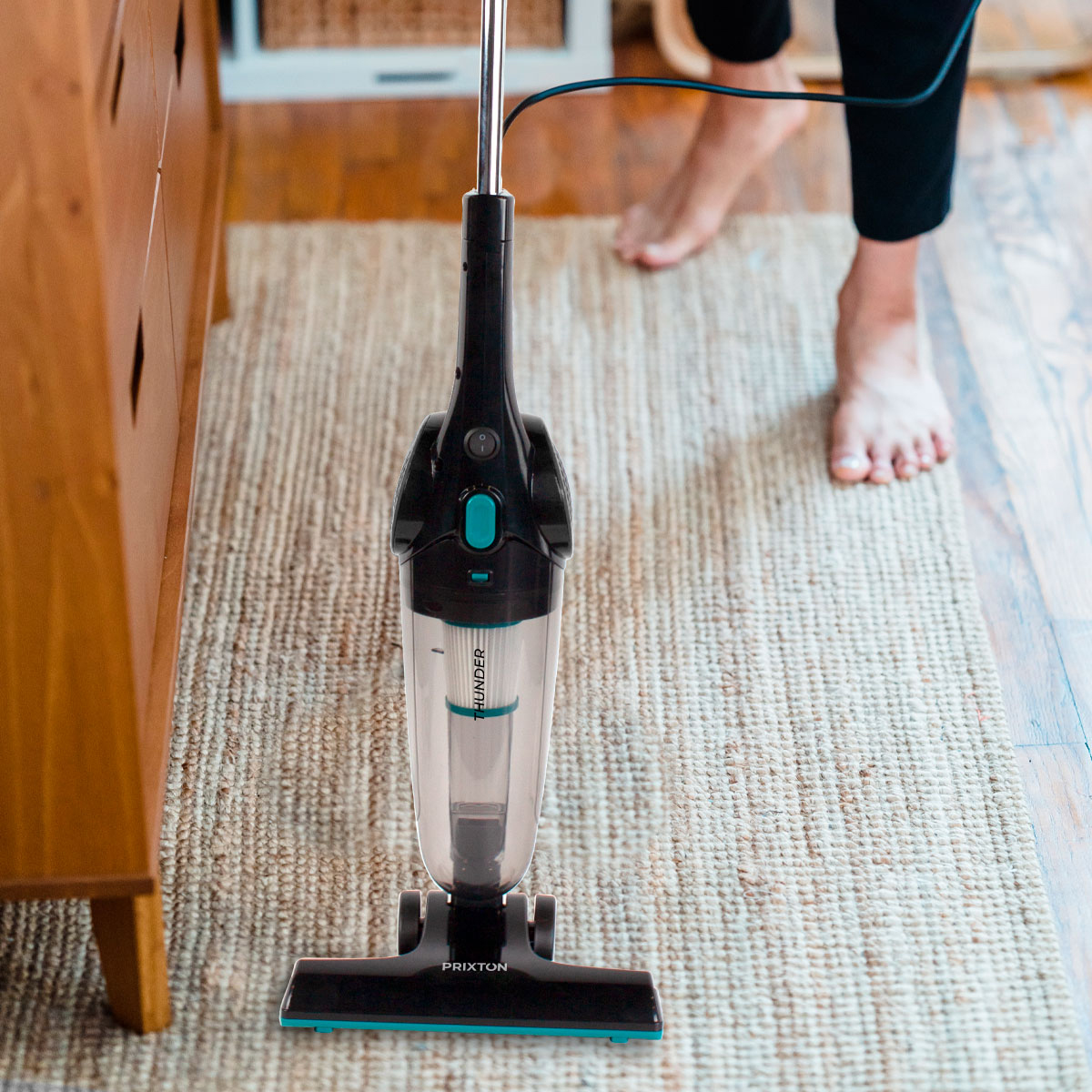 Czarny i turkusowy odkurzacz ręczny na dywanie. Stopy osoby widoczne w tle.