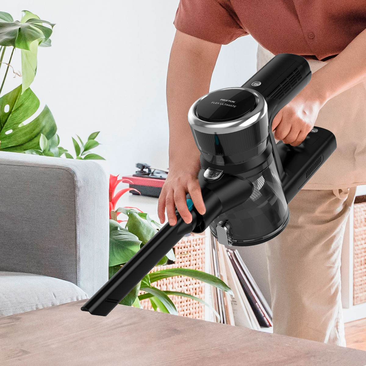 Osoba używa czarnego odkurzacza. Tło przedstawia kanapę i rośliny.