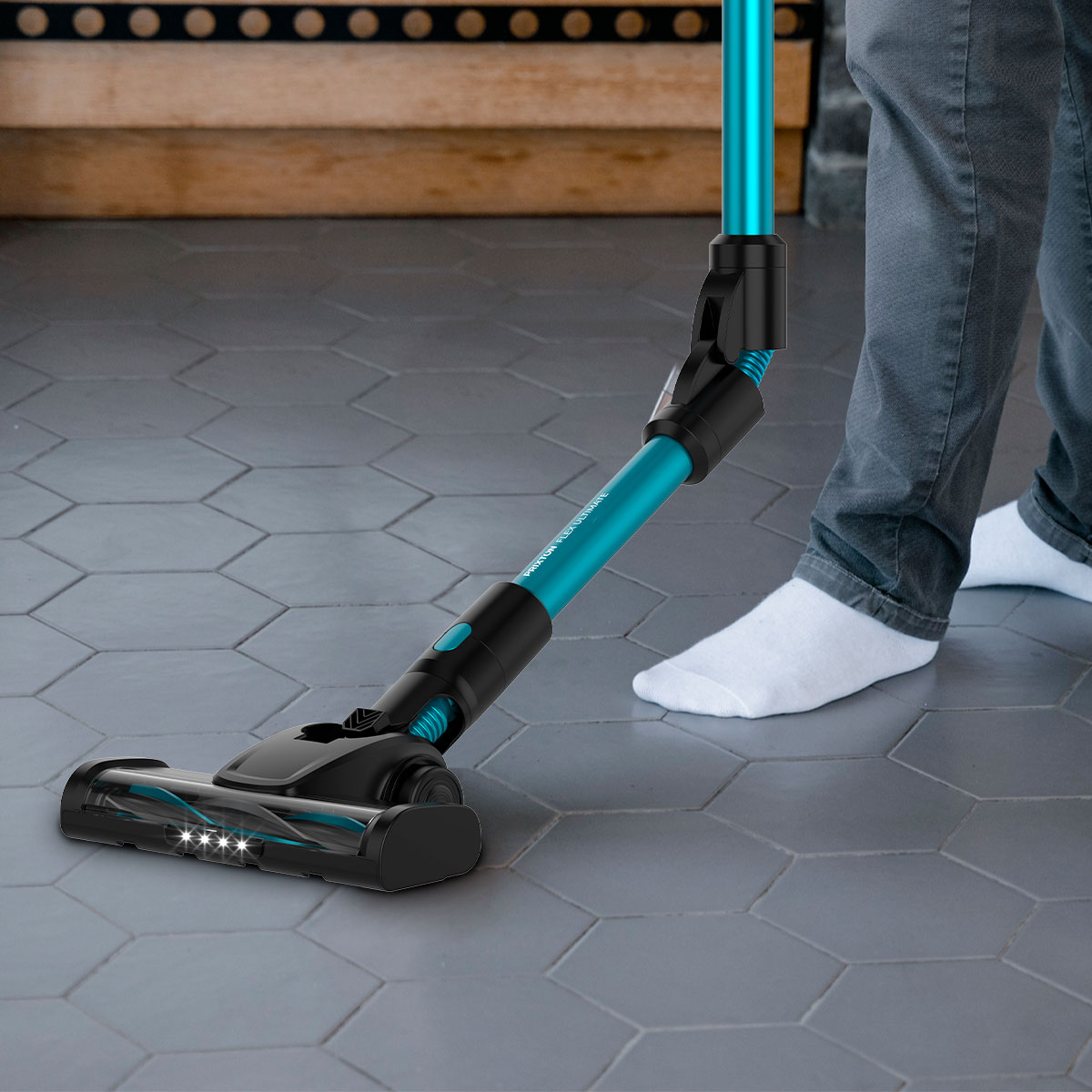 Osoba używająca niebiesko-czarnego odkurzacza na kafelkach, w szarych spodniach i białych skarpetach.