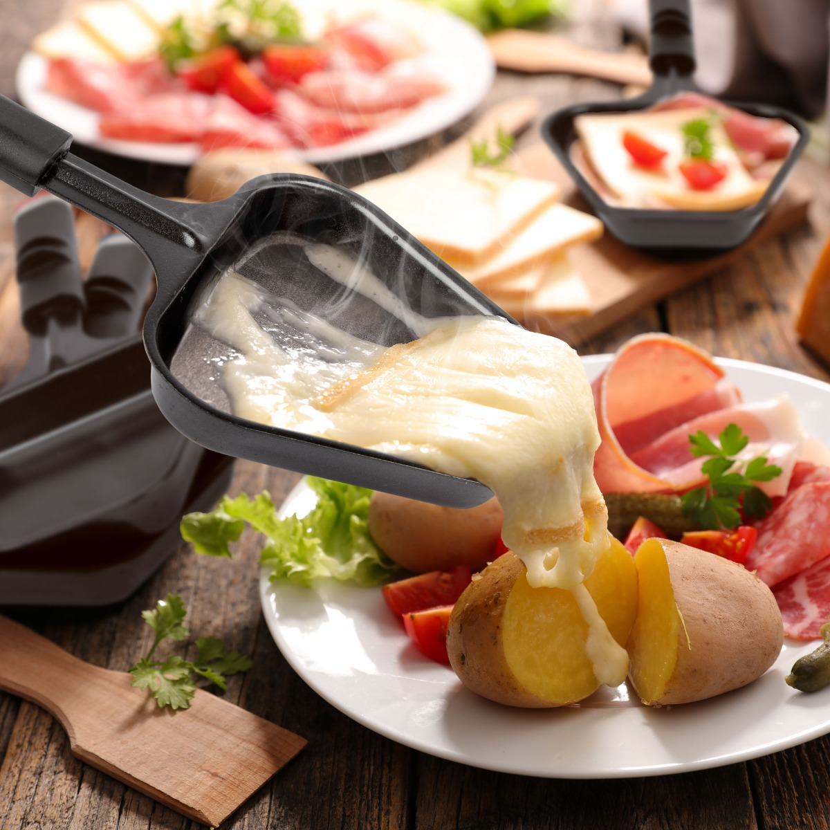 Raclette-Käse schmilzt auf einer Kartoffel. Serviert mit anderen Speisen auf einem weißen Teller. Holztisch.