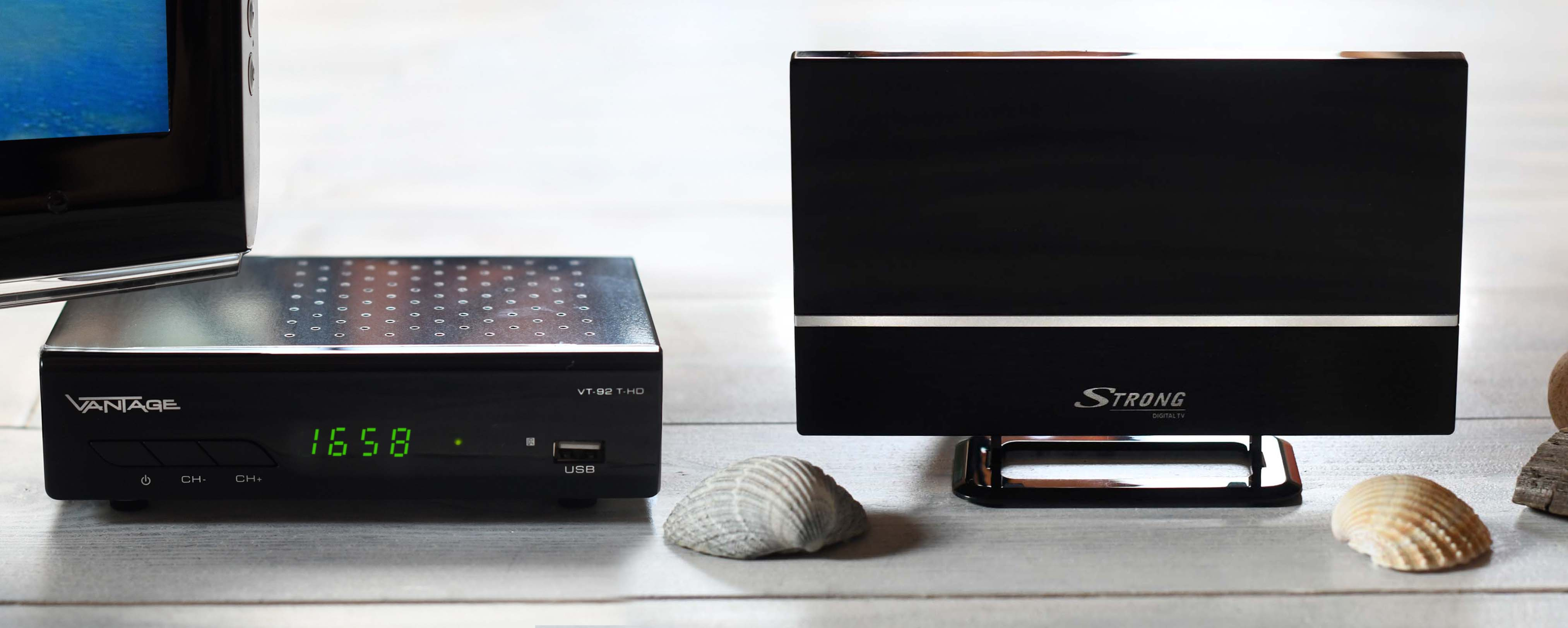 Zwei schwarze TV-Boxen mit einem Fernseher. Weißer Hintergrund mit ein paar Muscheln.