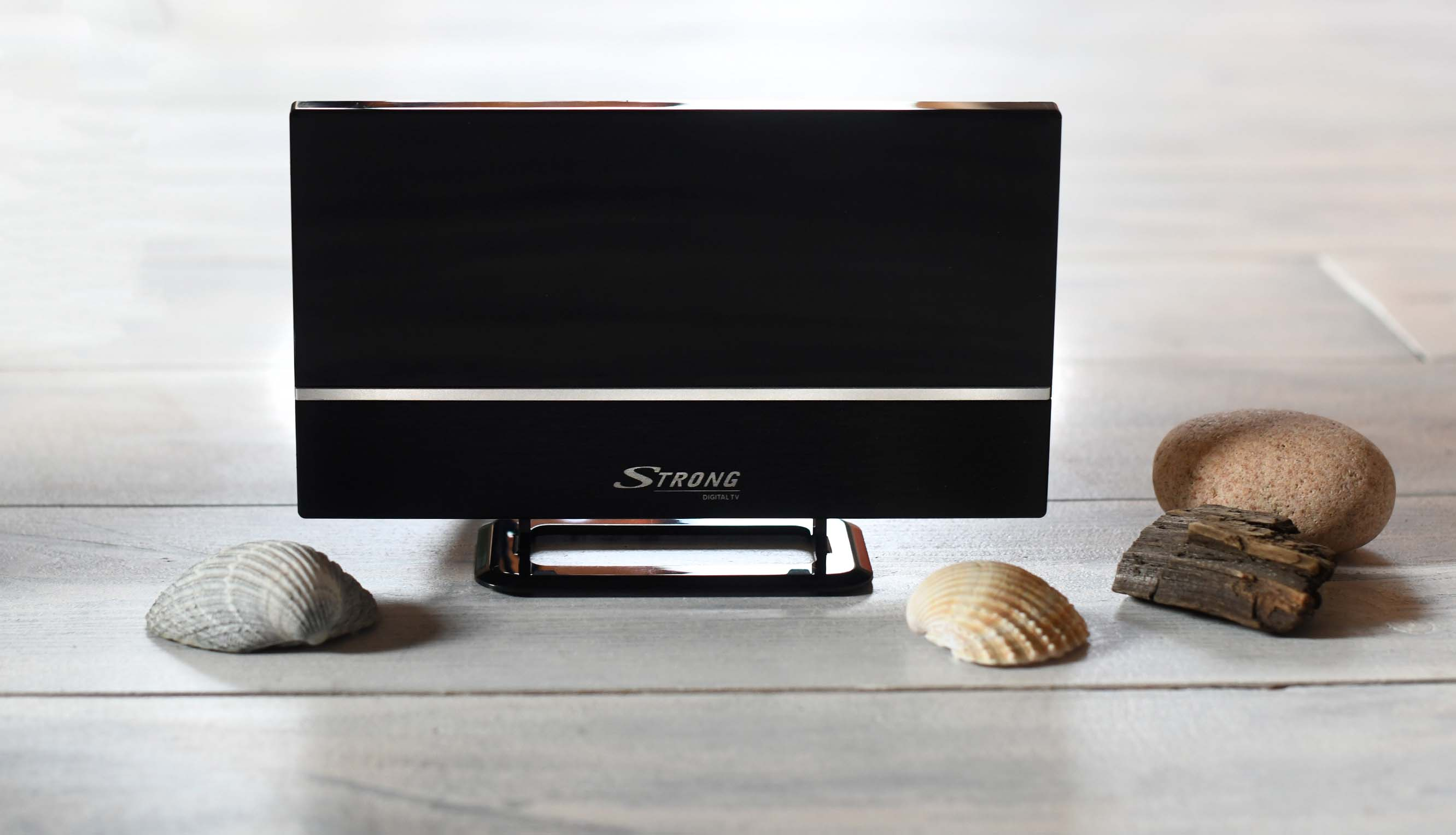 Ein schwarzer digitaler TV-Receiver auf Holz mit Muscheln und Treibholz.