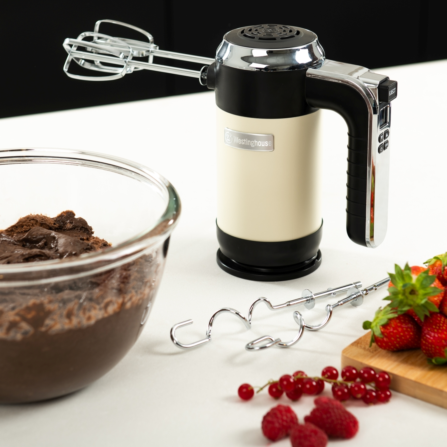 Handmixer mit Schüssel mit Schokolade, Erdbeeren und anderen Beeren auf weißer Oberfläche.