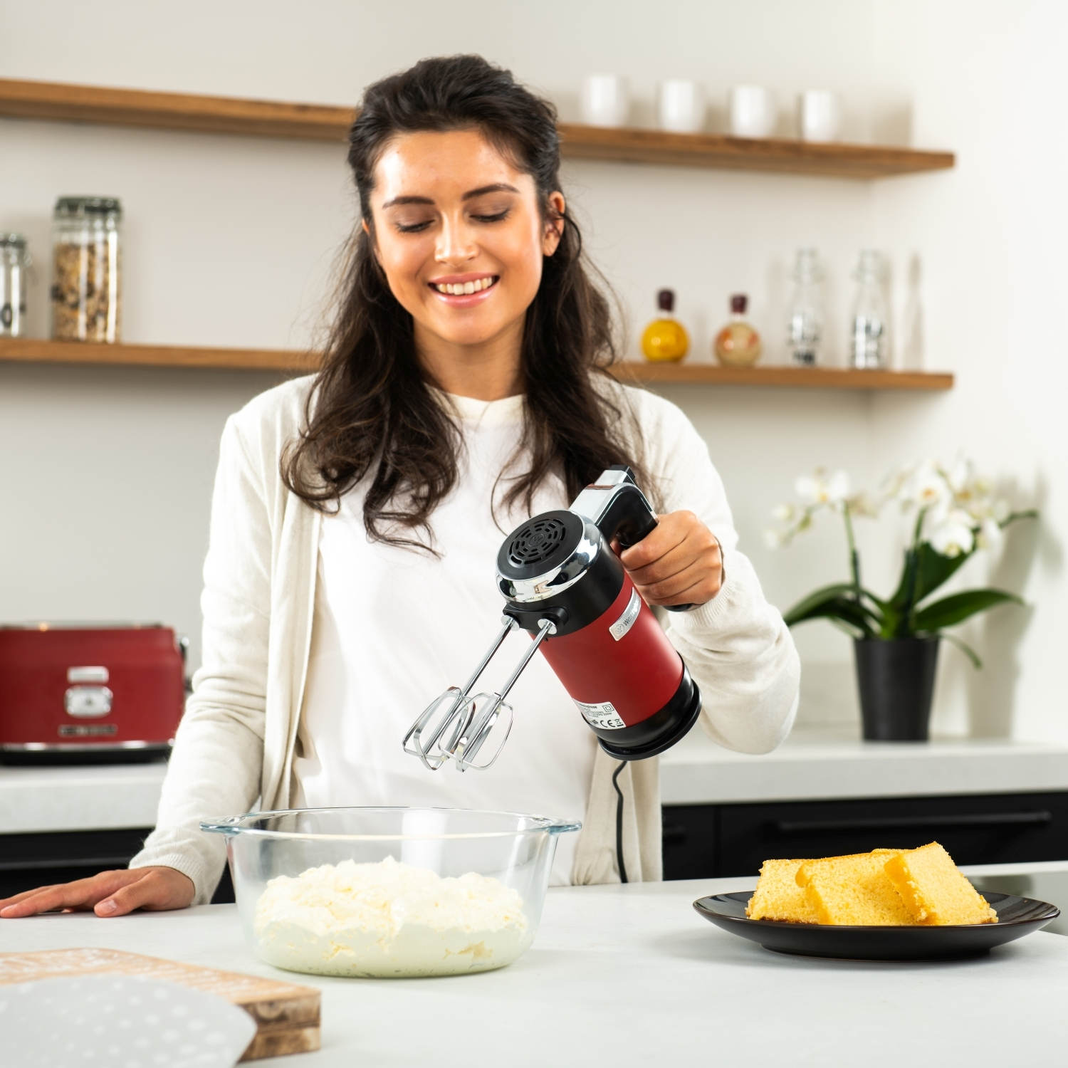 Eine lächelnde Frau, die mit einem roten Handmixer Sahne in einer Schüssel aufschlägt.