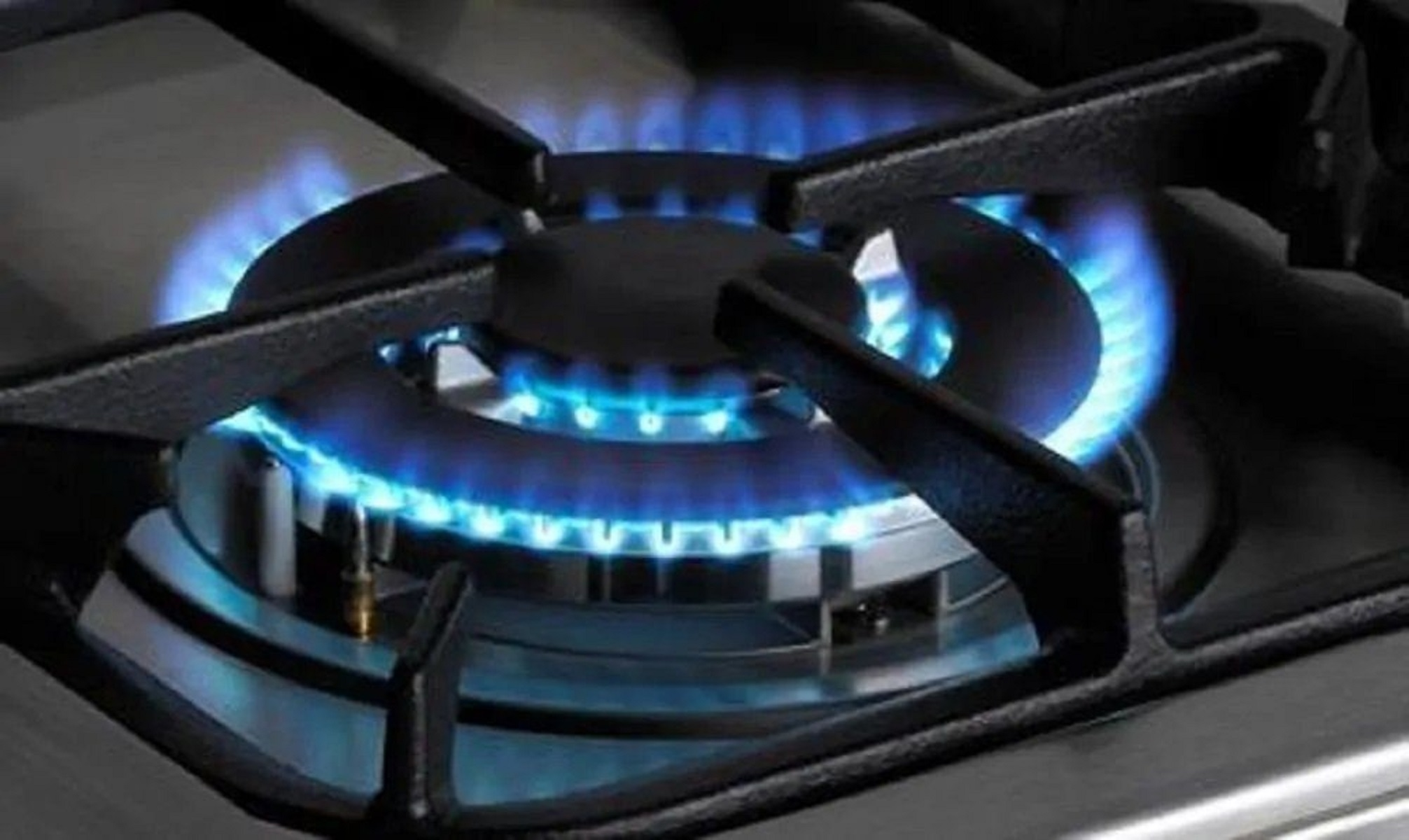 Nahaufnahme eines Gasherd-Brenners mit blauen Flammen. Der Brenner ist schwarz, der Herd ist Edelstahl.