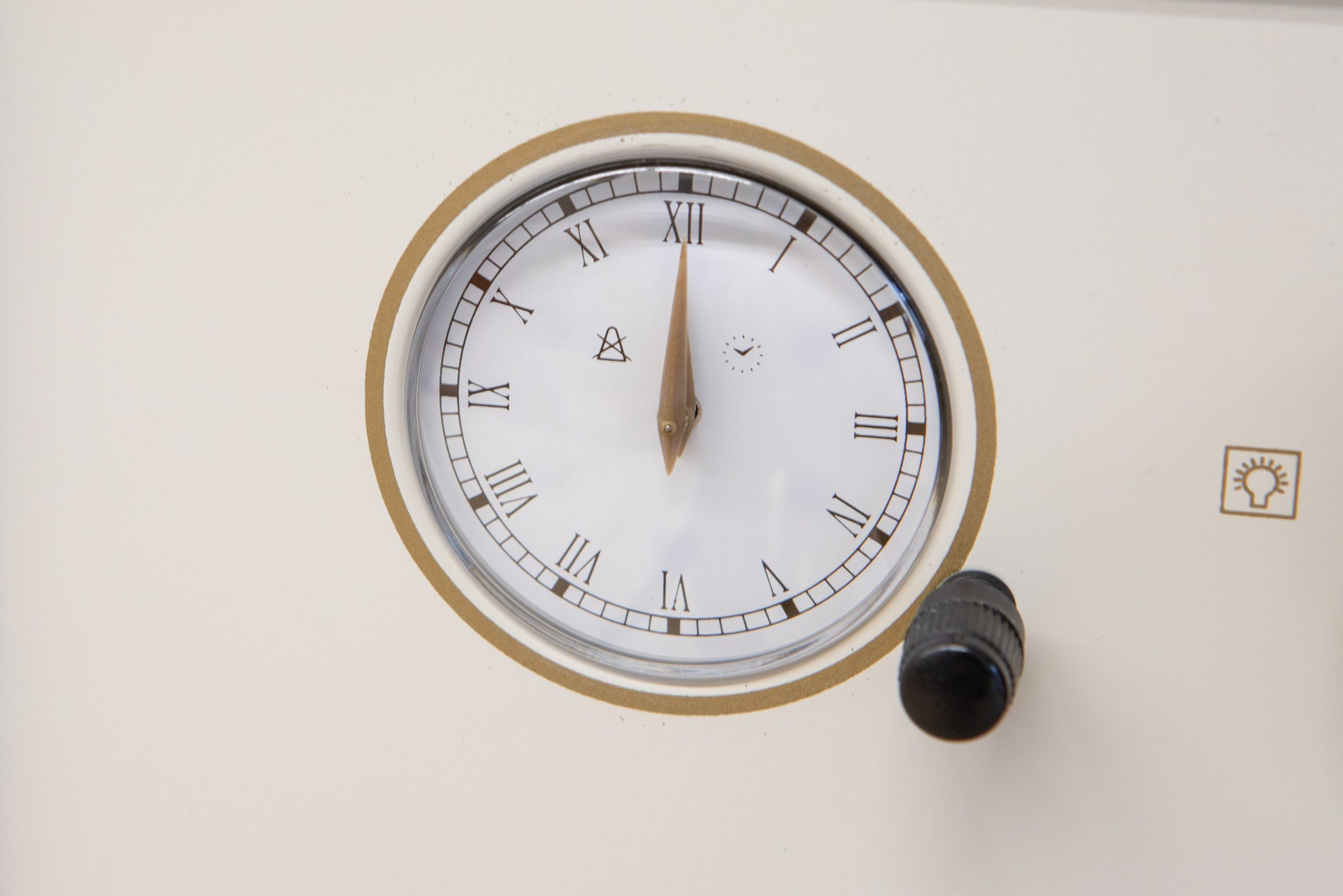 Weiße Uhr mit römischen Ziffern, schwarzem Knopf und einer Glühbirne.