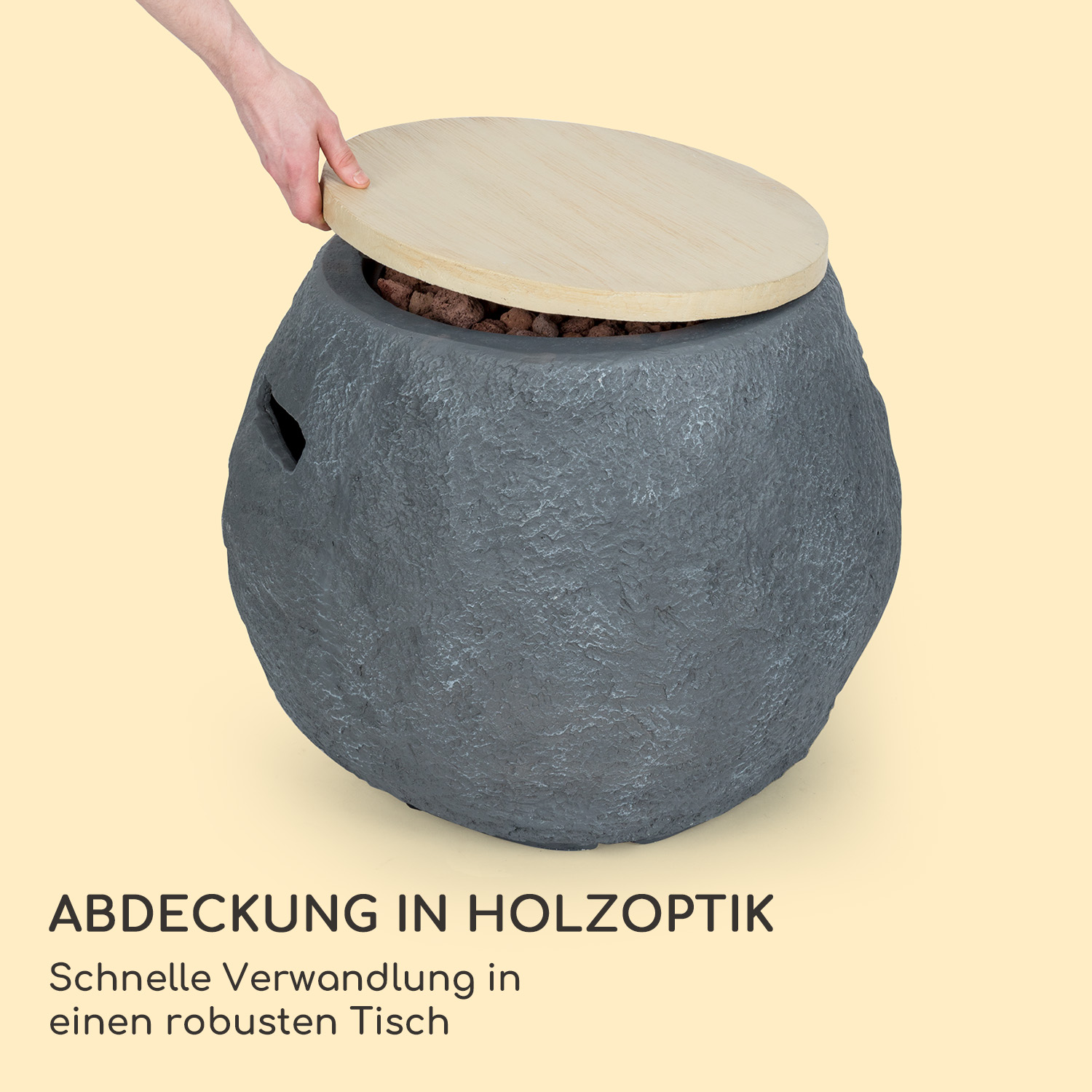 Eine Hand hebt einen Holzdeckel von einem grauen, steinartigen Außenfeuerkorb auf hellgelbem Hintergrund.