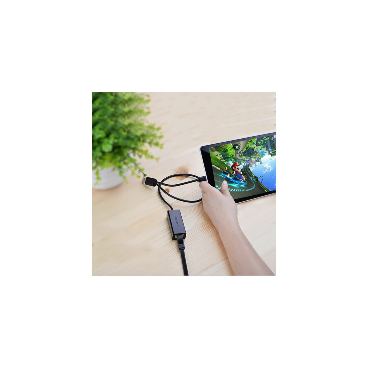 Tablet, USB kablosuyla siyah bir adaptöre bağlı. Oyun ekran üzerinde görüntüleniyor.