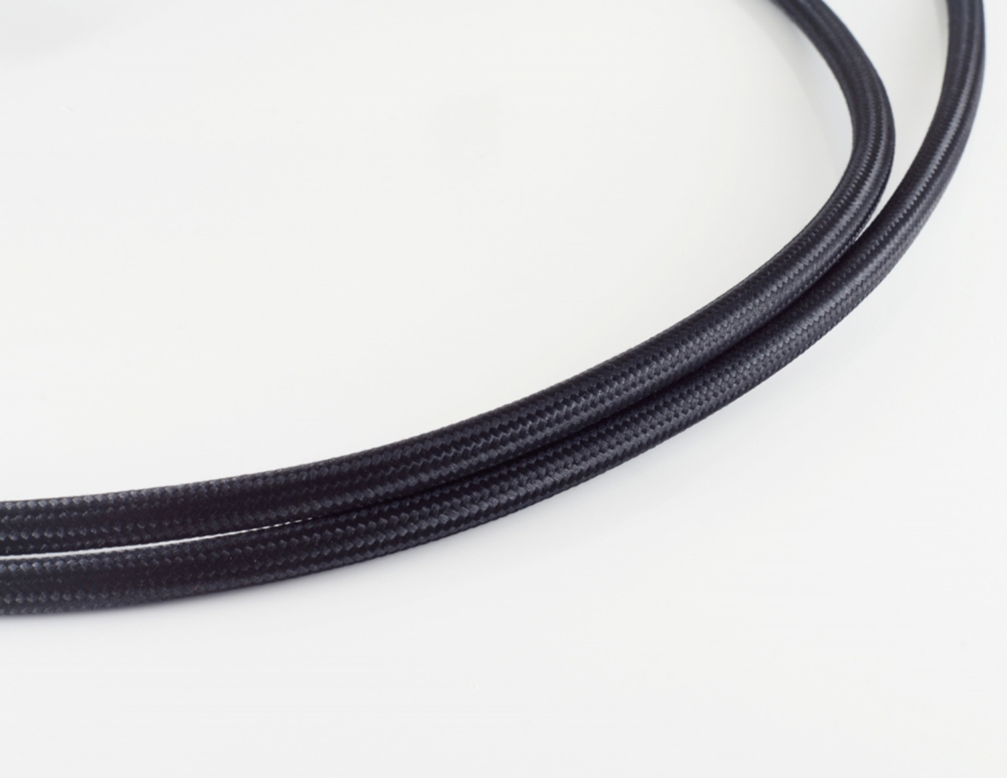 Zwei schwarze, geflochtene Kabel, leicht gekrümmt, vor weißem Hintergrund. Nahaufnahme.