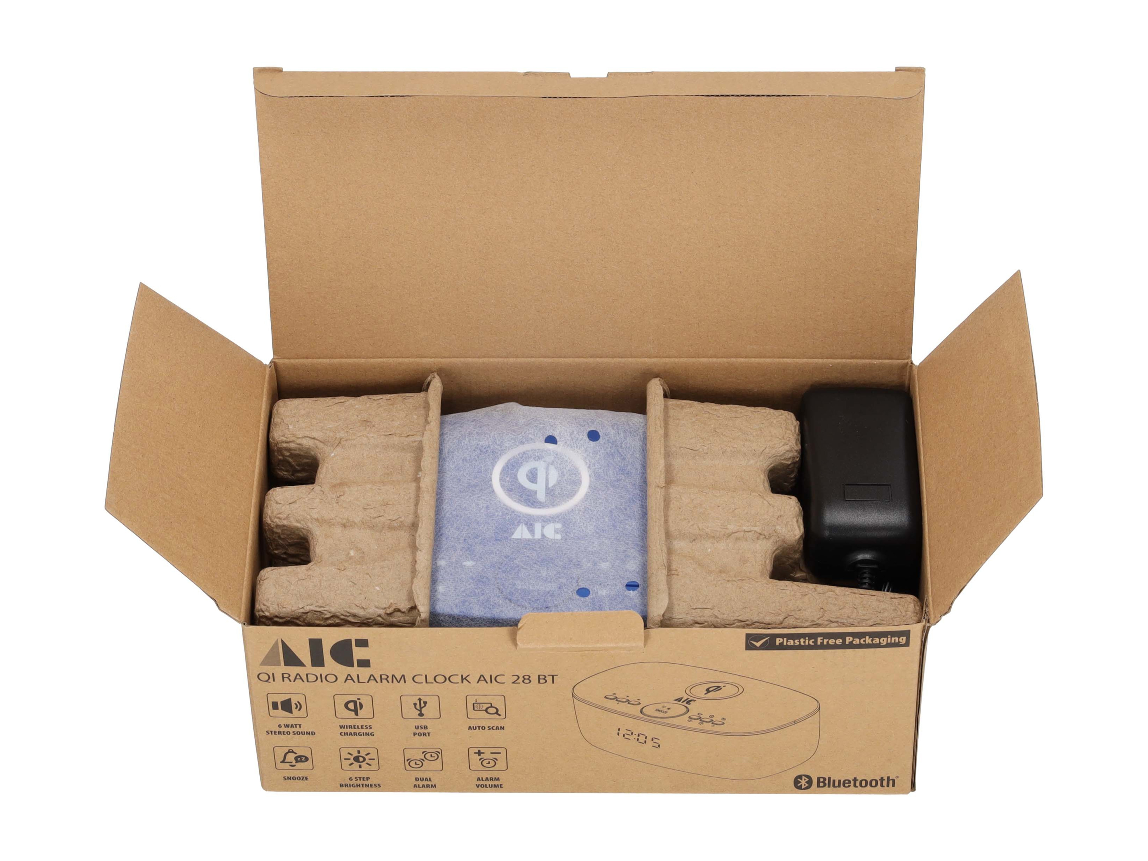 Wecker in einer Schachtel. Die Schachtel ist offen, mit Verpackungsmaterial und einem Adapter.