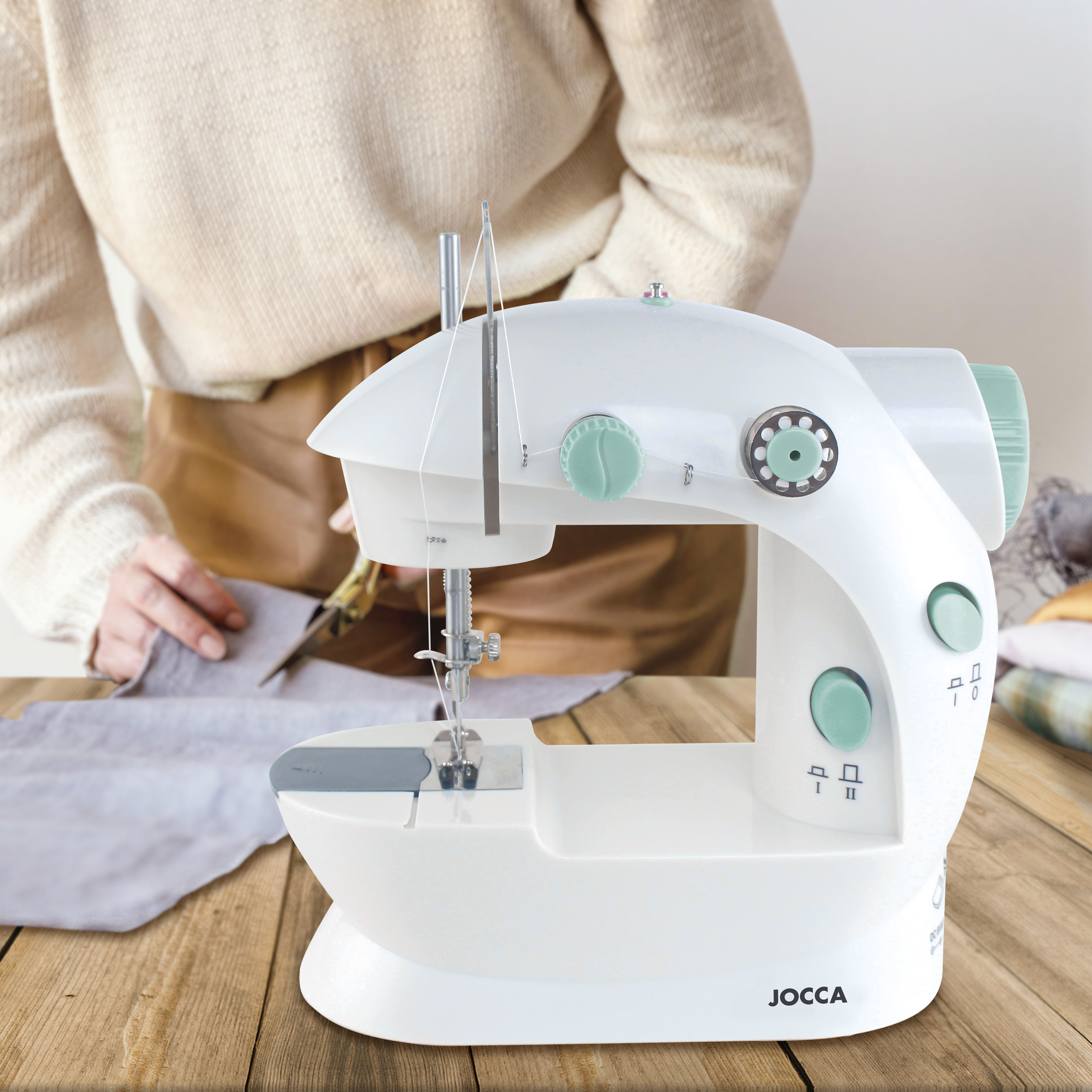 Eine weiße Nähmaschine auf einem Holztisch mit einer Person, die im Hintergrund näht.