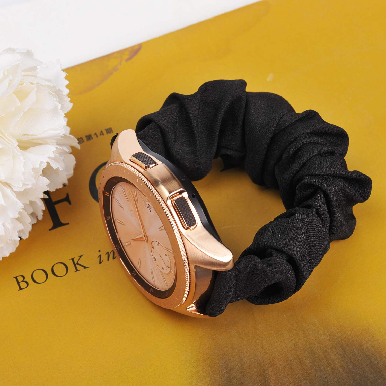 Eine goldene Smartwatch mit schwarzem Scrunchie-Band auf gelbem Untergrund.