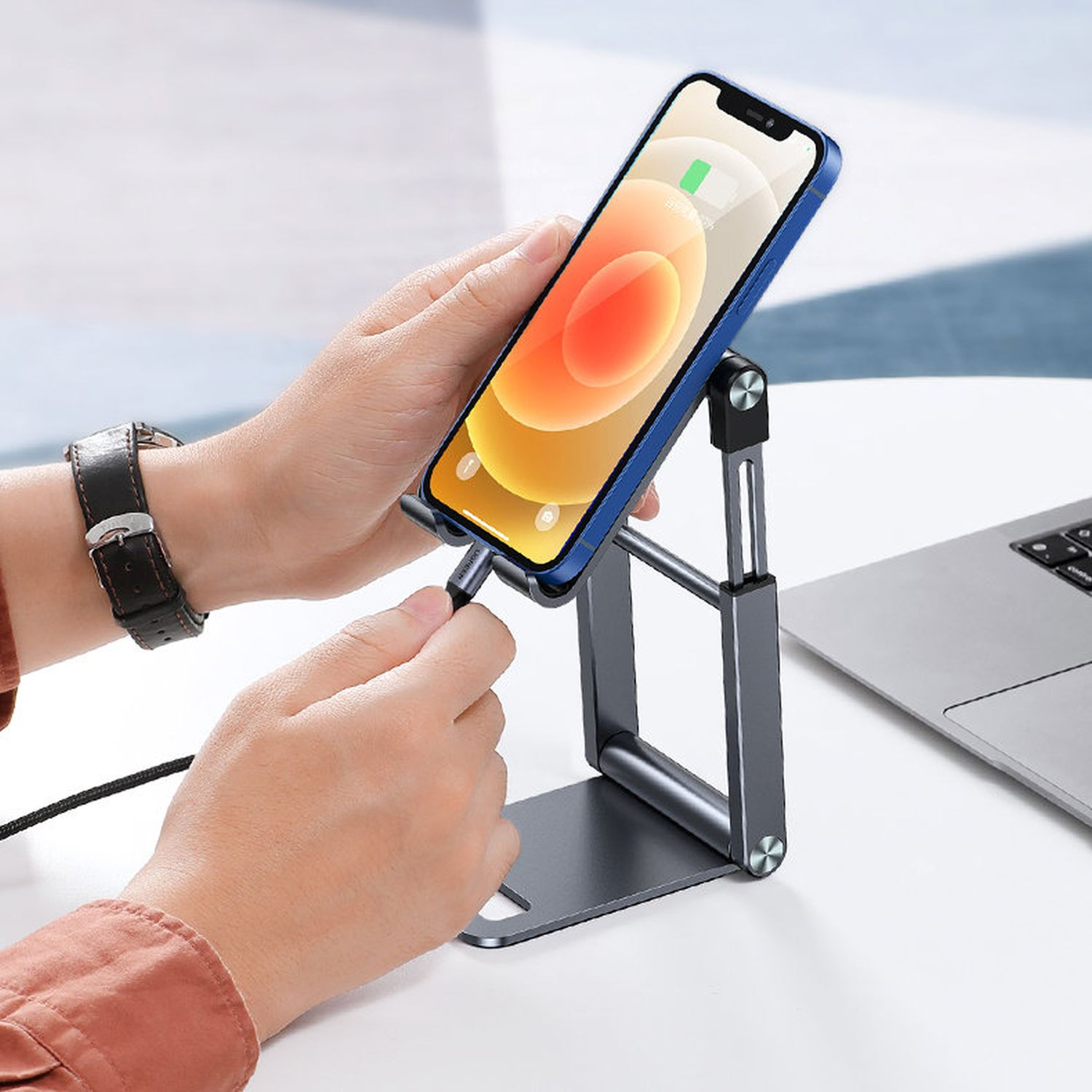 Eine Person, die ein Telefon auf einem grauen Ständer hält, während sie ein Ladekabel einsteckt.