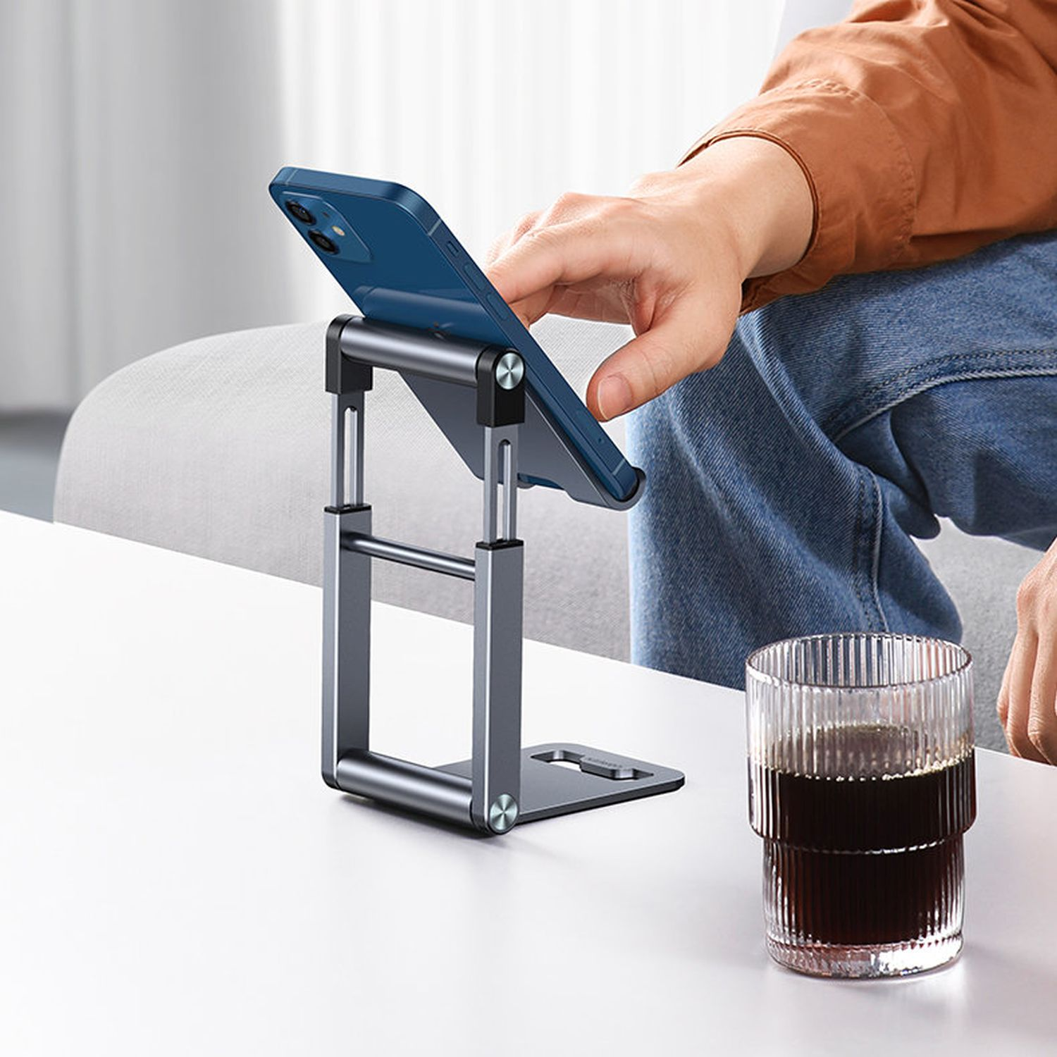 Telefon auf einem Ständer, die Hand einer Person justiert das Telefon. Ein Glas steht daneben auf einem Tisch.