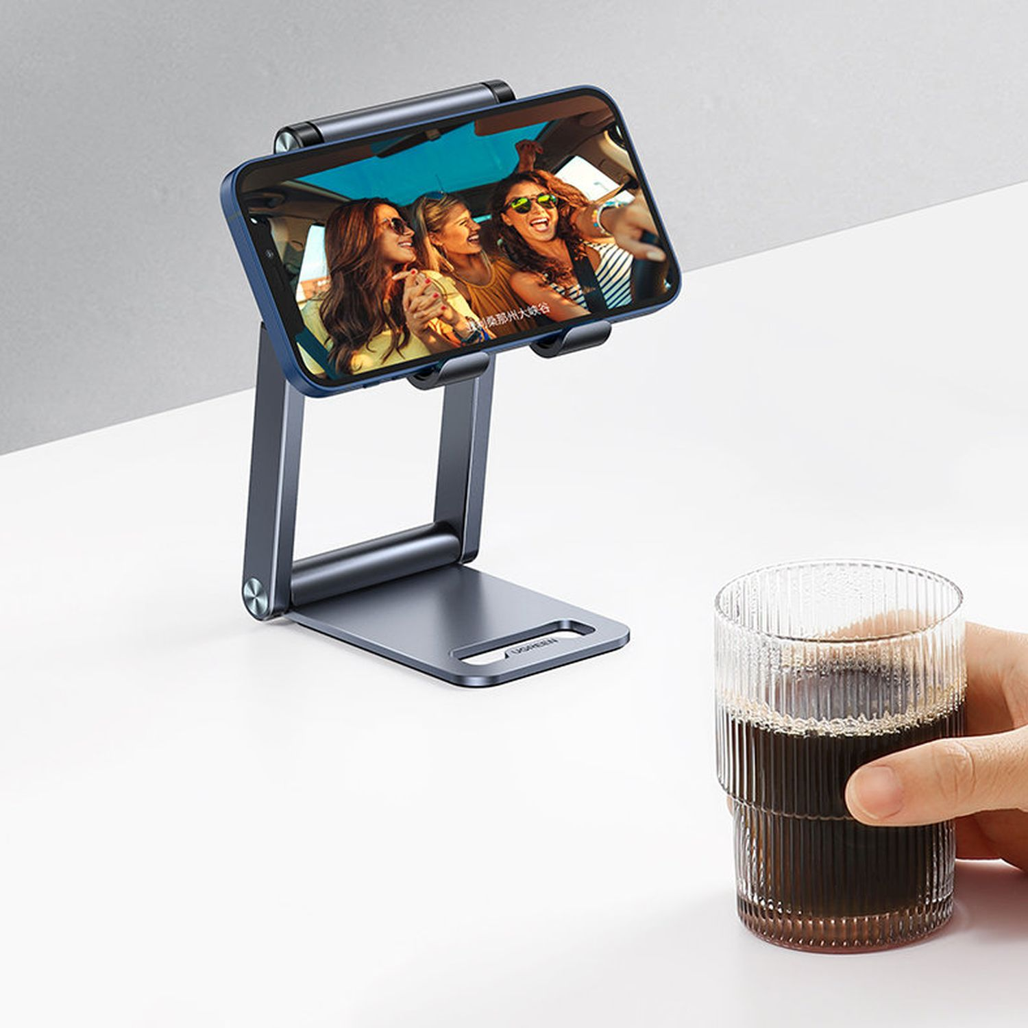 Telefonständer, der ein Telefon mit einer Personengruppe hält. Ein Glas Kaffee steht daneben.