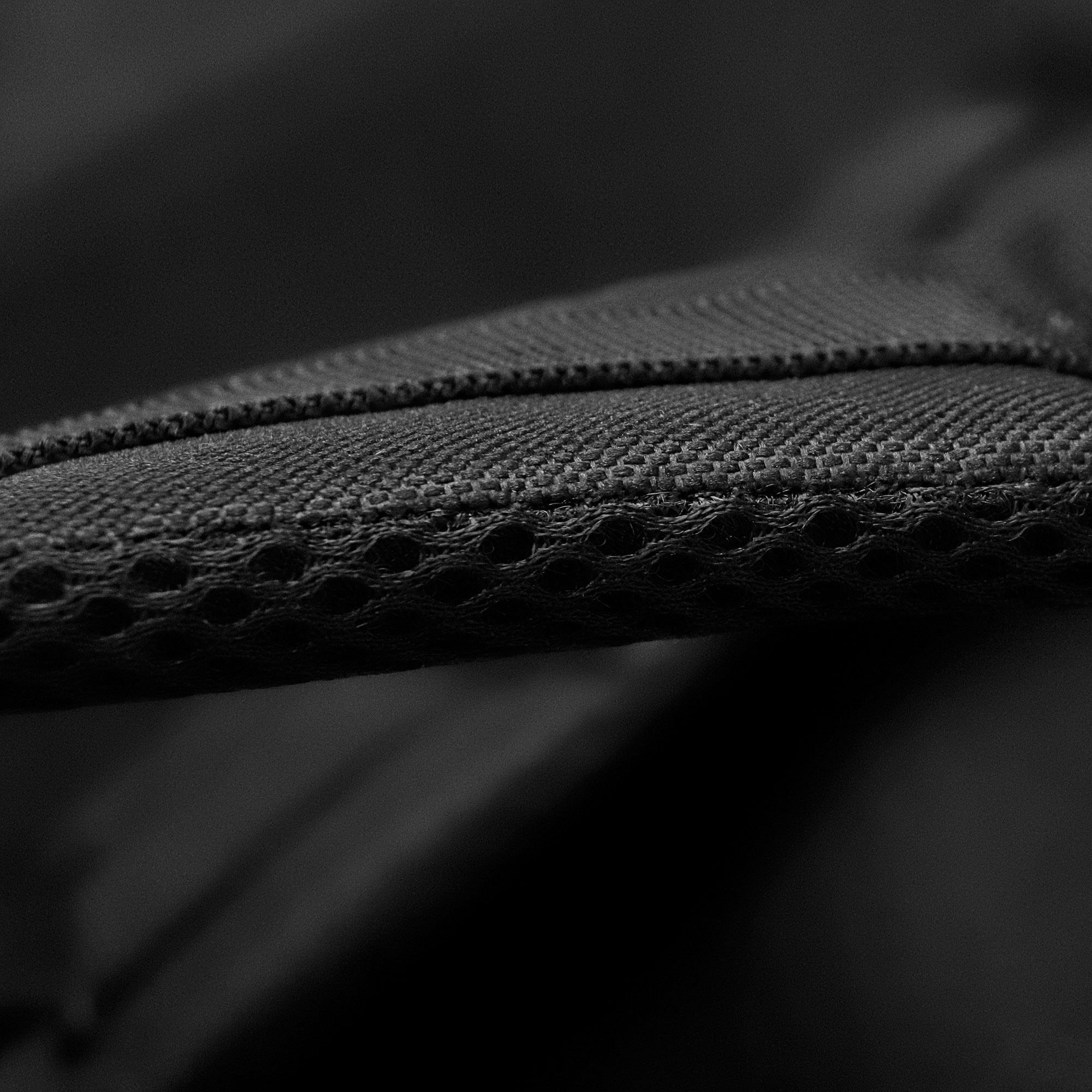 Gros plan sur tissu noir avec surface texturée et petits trous. Mise au point sur le bord et la couture.