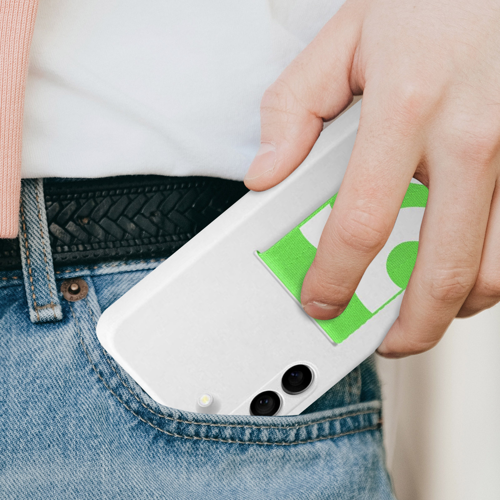 Ręka trzymająca biały telefon z zieloną kieszenią w kieszeni dżinsów.