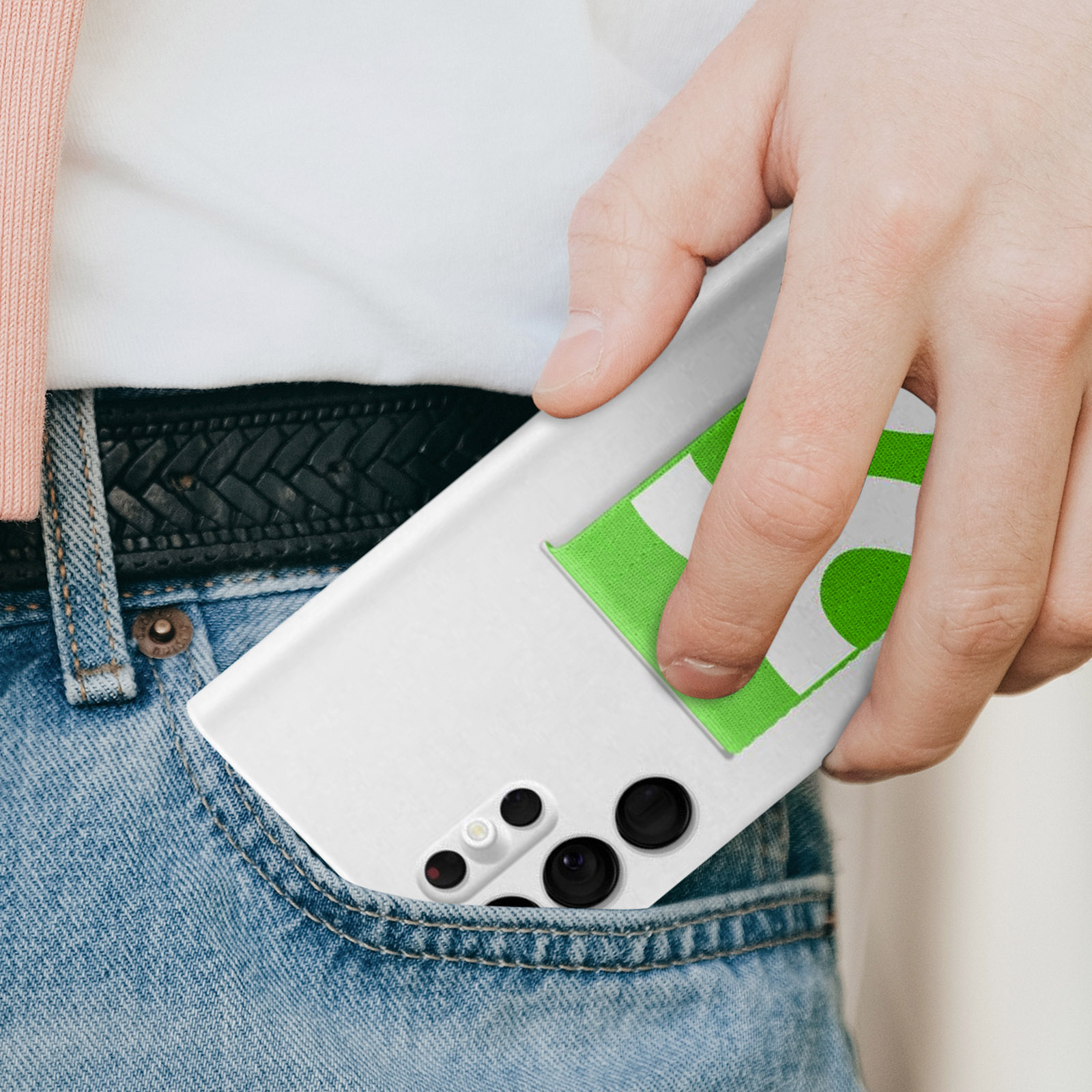 Die Hand einer Person, die ein weißes Telefon mit einem grünen Aufkleber in eine Jeans-Tasche steckt.