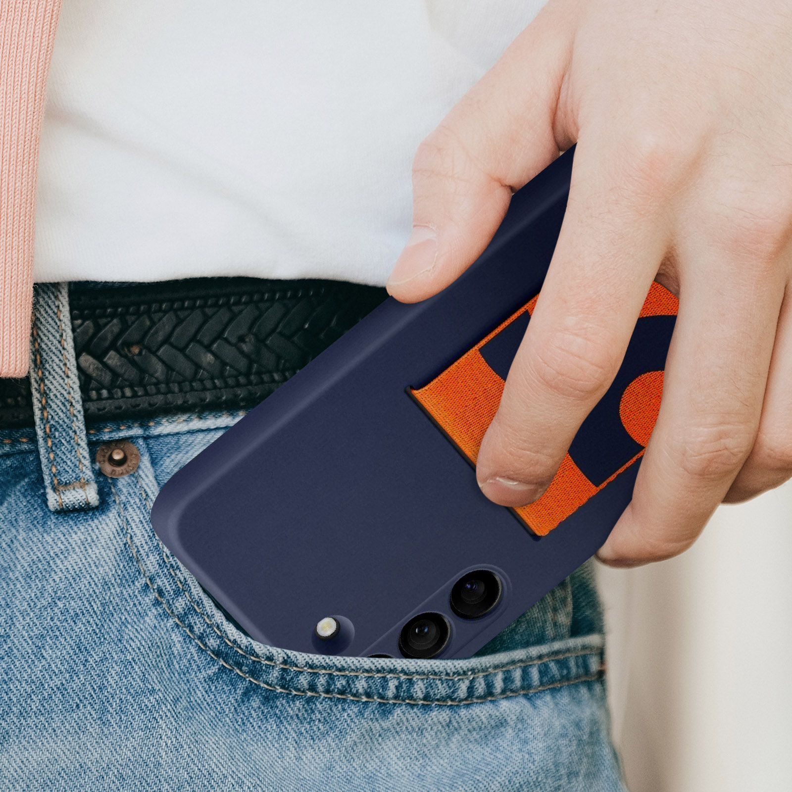 Een hand die een telefoon in een zak steekt. De telefoon heeft een oranje en blauw ontwerp.
