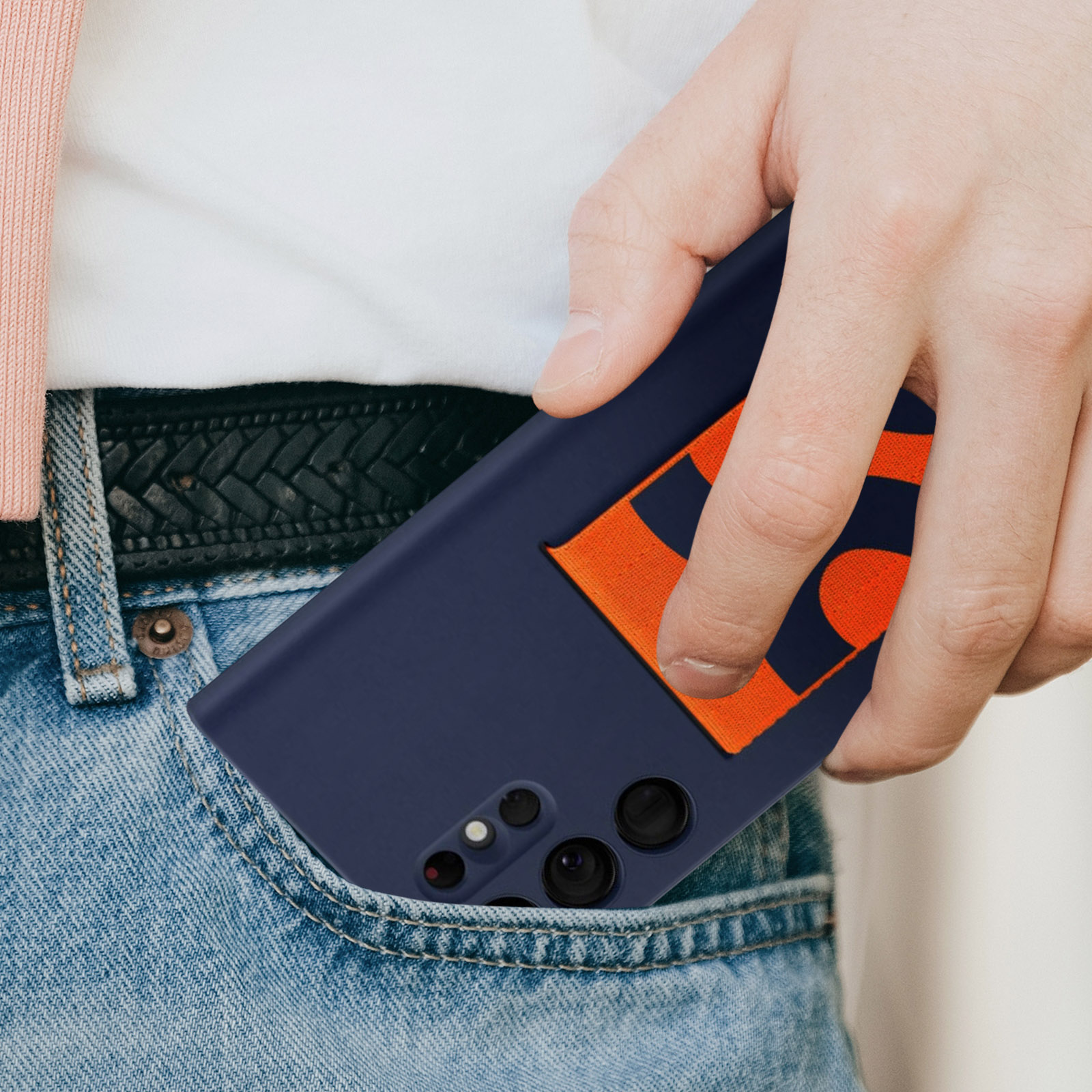 Mano de una persona en un bolsillo de jeans sosteniendo un teléfono en una funda azul marino.