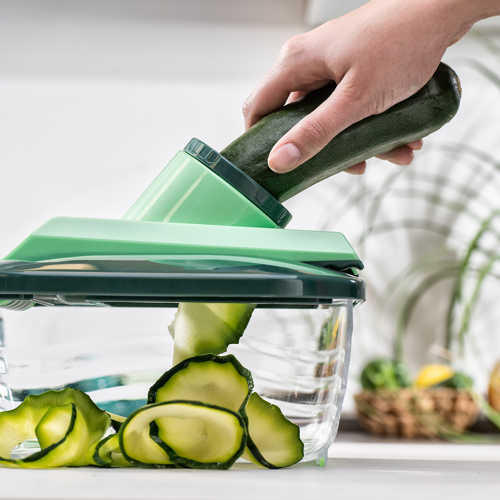 Eine Hand hält eine Zucchini, um sie mit einem grünen Spiralschneider zu schneiden. Zucchini wird in Spiralen geschnitten.