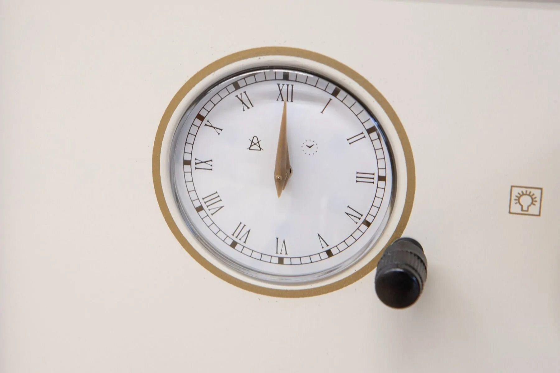 Eine Uhr zeigt 12:00 Uhr an, ein Knopf und ein Glühbirnensymbol sind sichtbar.