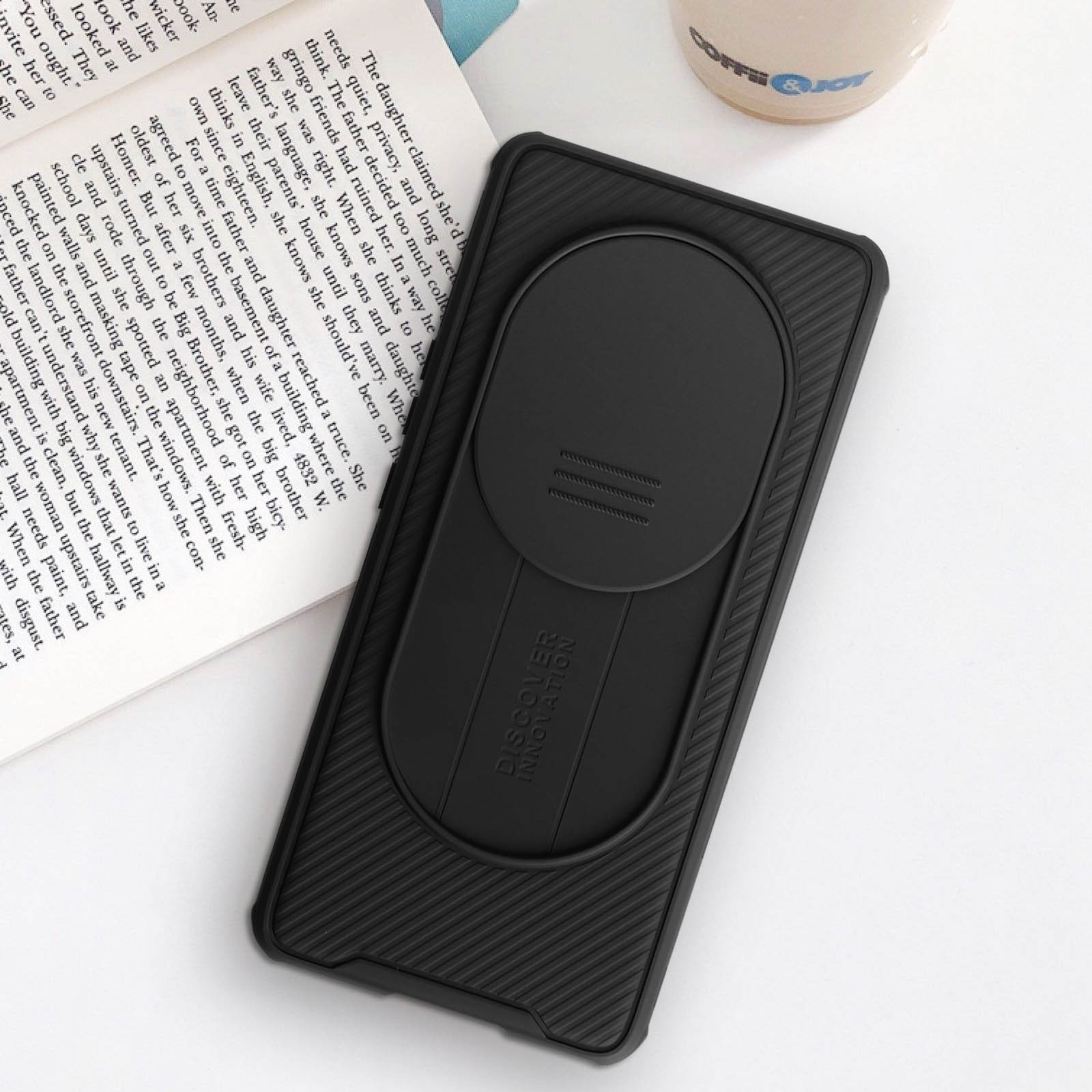 Custodia nera per telefono con copertura scorrevole per la fotocamera. La custodia è su un libro, sfondo scuro.