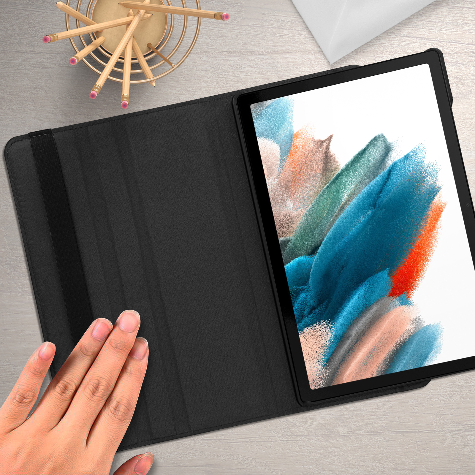 Tablet con custodia nera. Una mano tocca la custodia. Sullo sfondo una scrivania con matite.