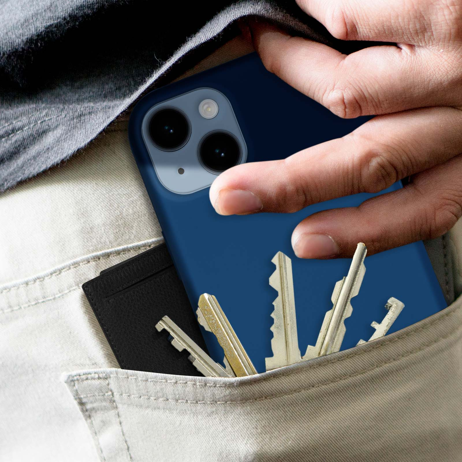 De hand van een persoon houdt een blauwe telefoon vast met een zwarte portemonnee en sleutels in de zak. Beige broek.