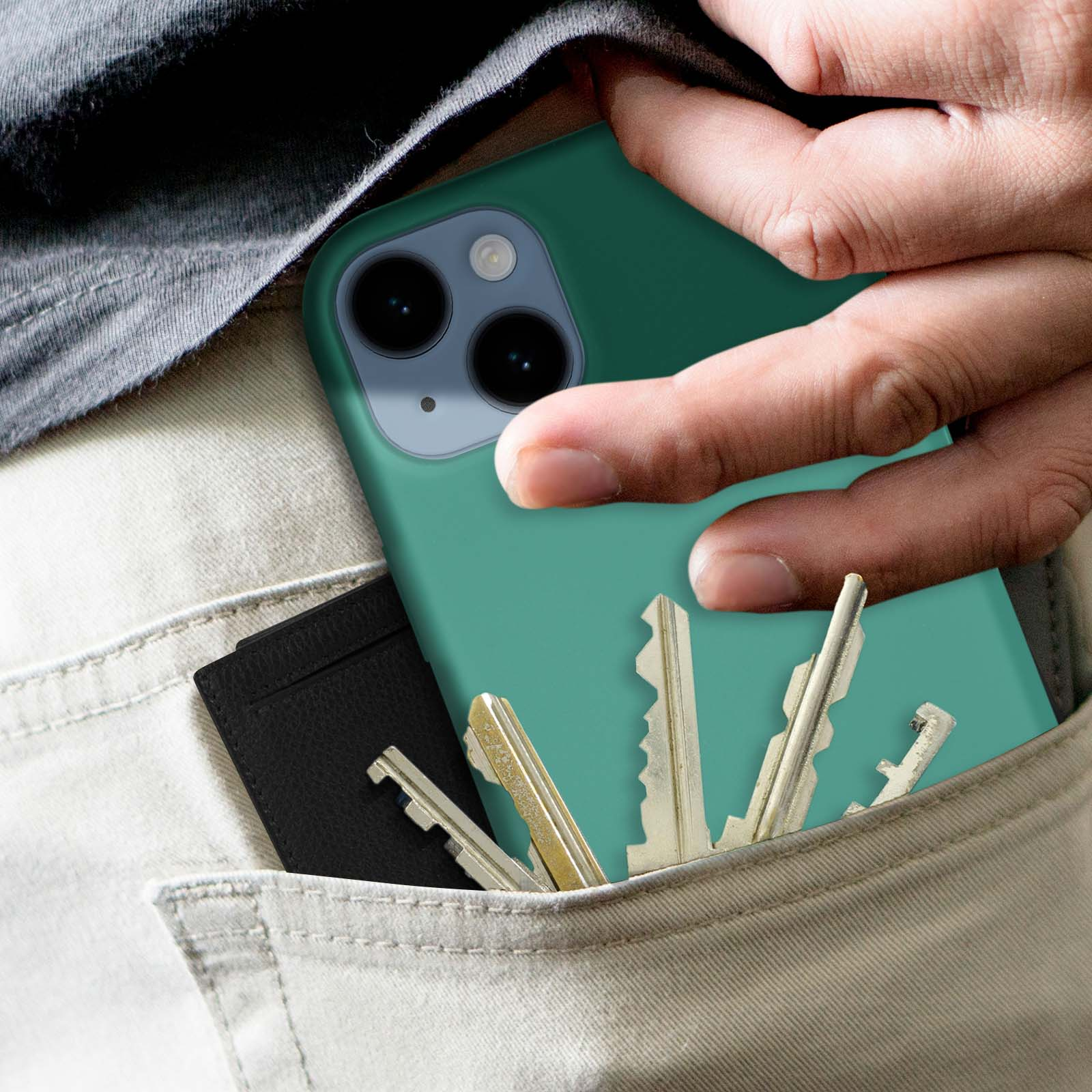 Main dans une poche, tenant un téléphone sarcelle et un porte-cartes noir avec des clés.