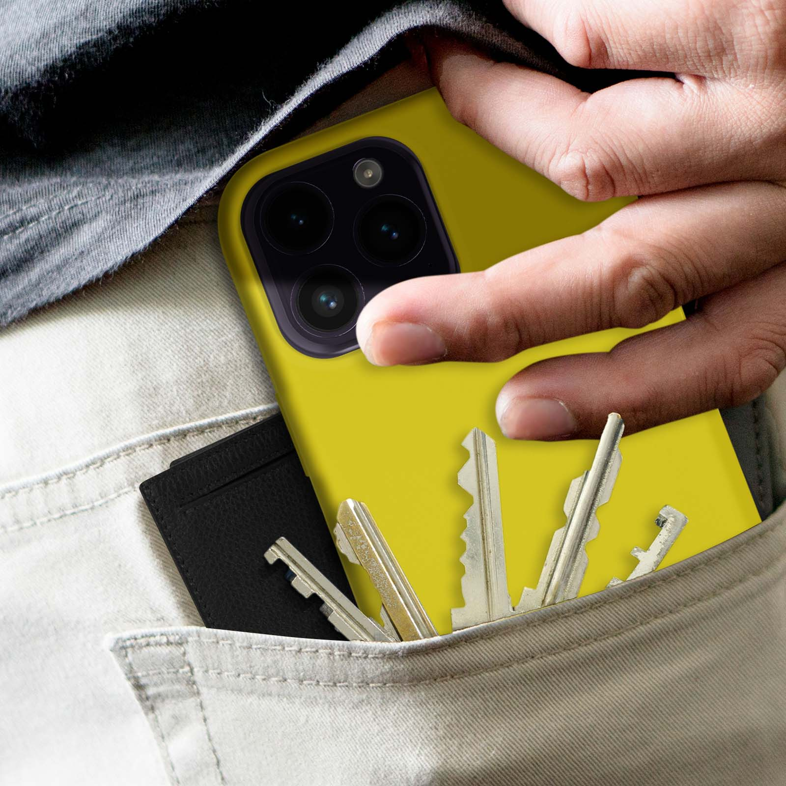 De hand van een persoon die een gele telefoonhoes vasthoudt met sleutels en een zwarte kaart in een zak.