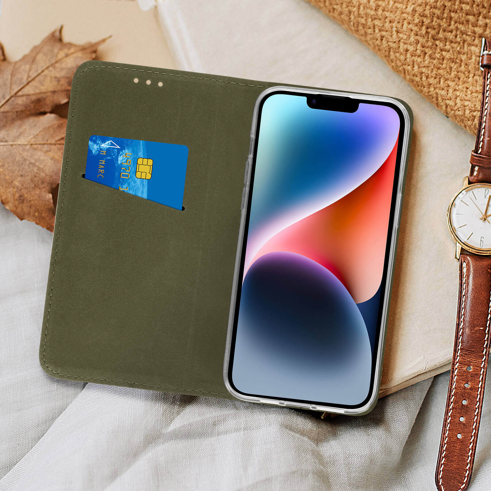 Custodia per telefono verde oliva con carta di credito e telefono, e un orologio, su una superficie beige.
