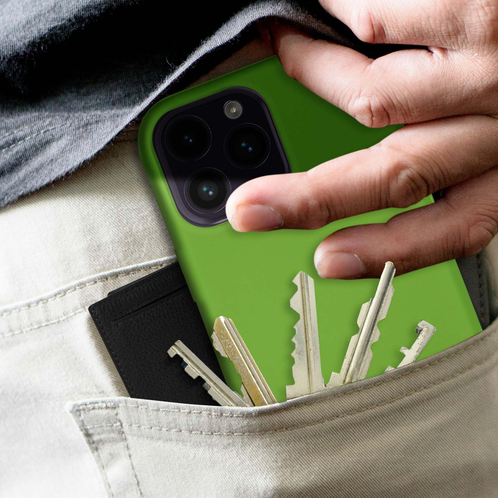 Main dans une poche tenant un téléphone avec une coque verte. Des clés et un porte-cartes noir sont également visibles.