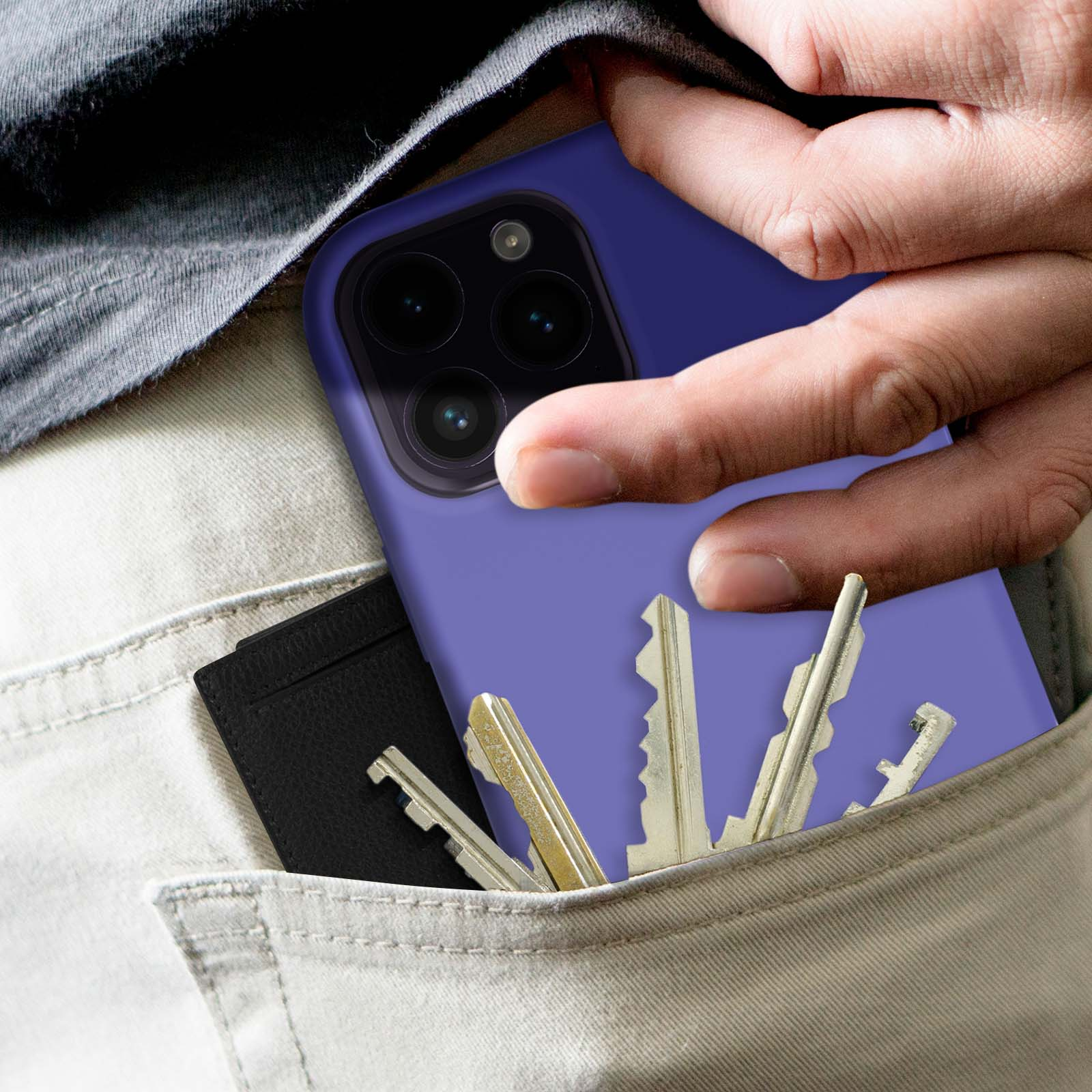 Étui de téléphone dans la poche avec des clés et un portefeuille noir. Main sur le téléphone. Pantalon gris.